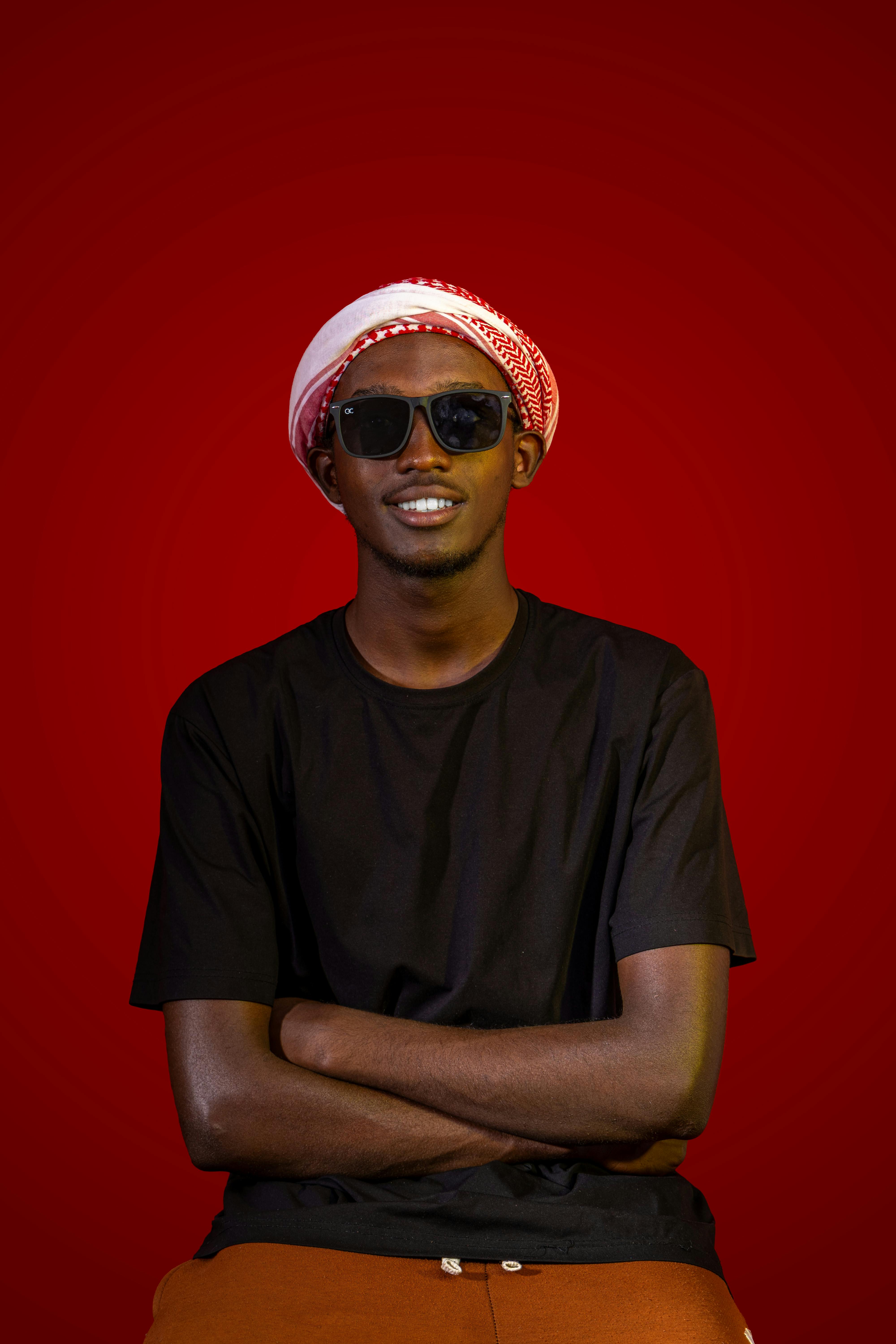 Безкоштовне Усміхнений чоловік у сонцезахисних окулярах та червоній хустці на червоному тлі. стокове фото