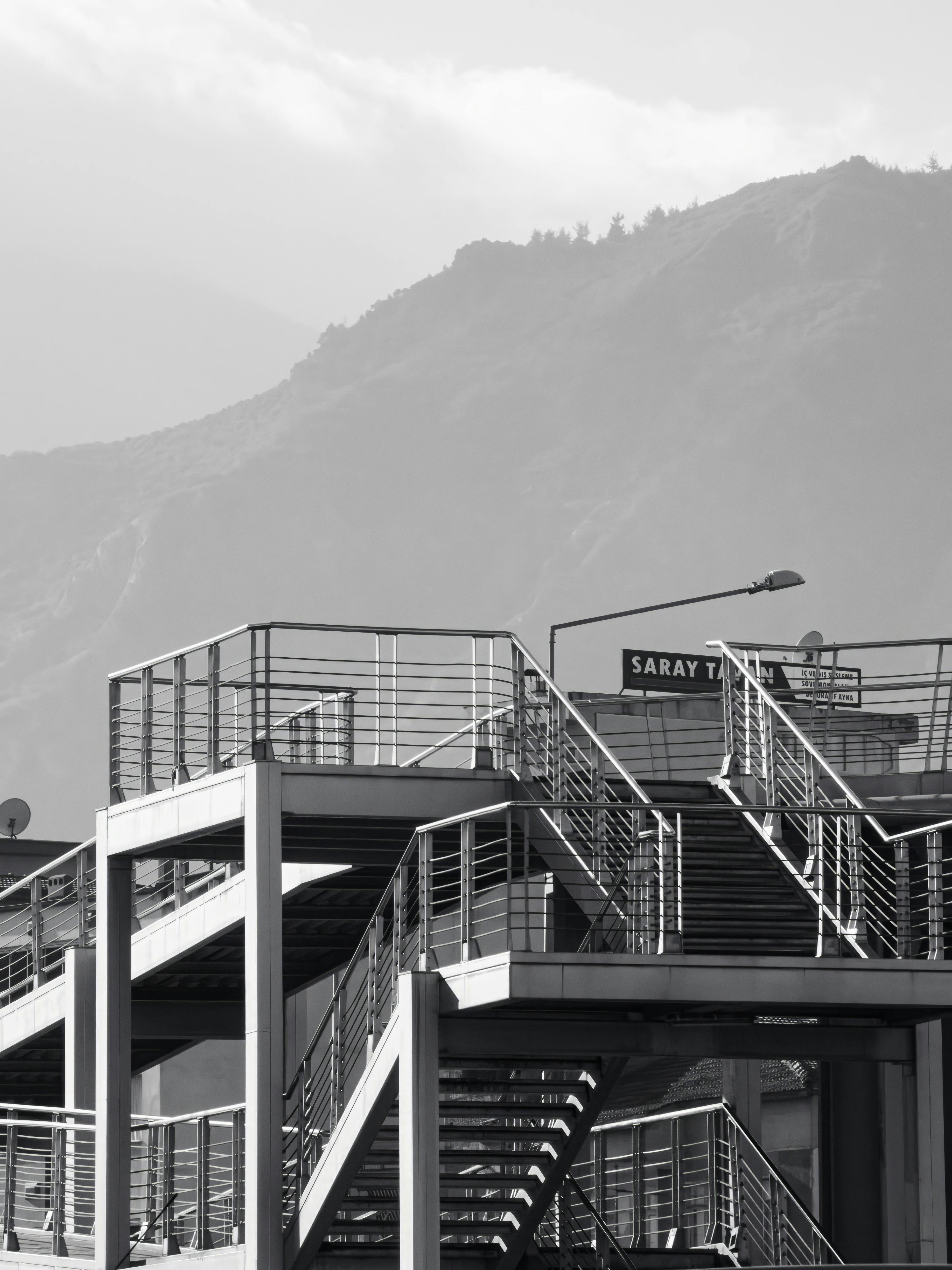 Δωρεάν Μονόχρωμη εικόνα μιας σύγχρονης σκάλας με φόντο ένα βουνό, που δημιουργεί μια εντυπωσιακή αντίθεση. Φωτογραφία από στοκ φωτογραφιών