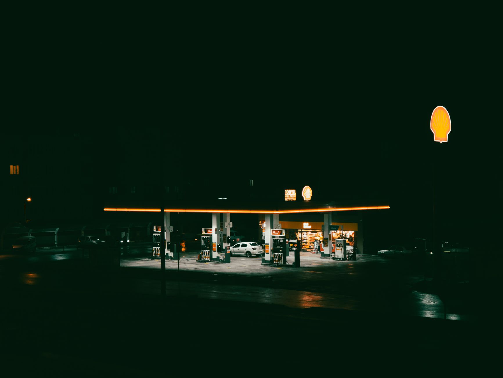 A brightly lit gas station at night, showcasing neon lights and empty pumps.