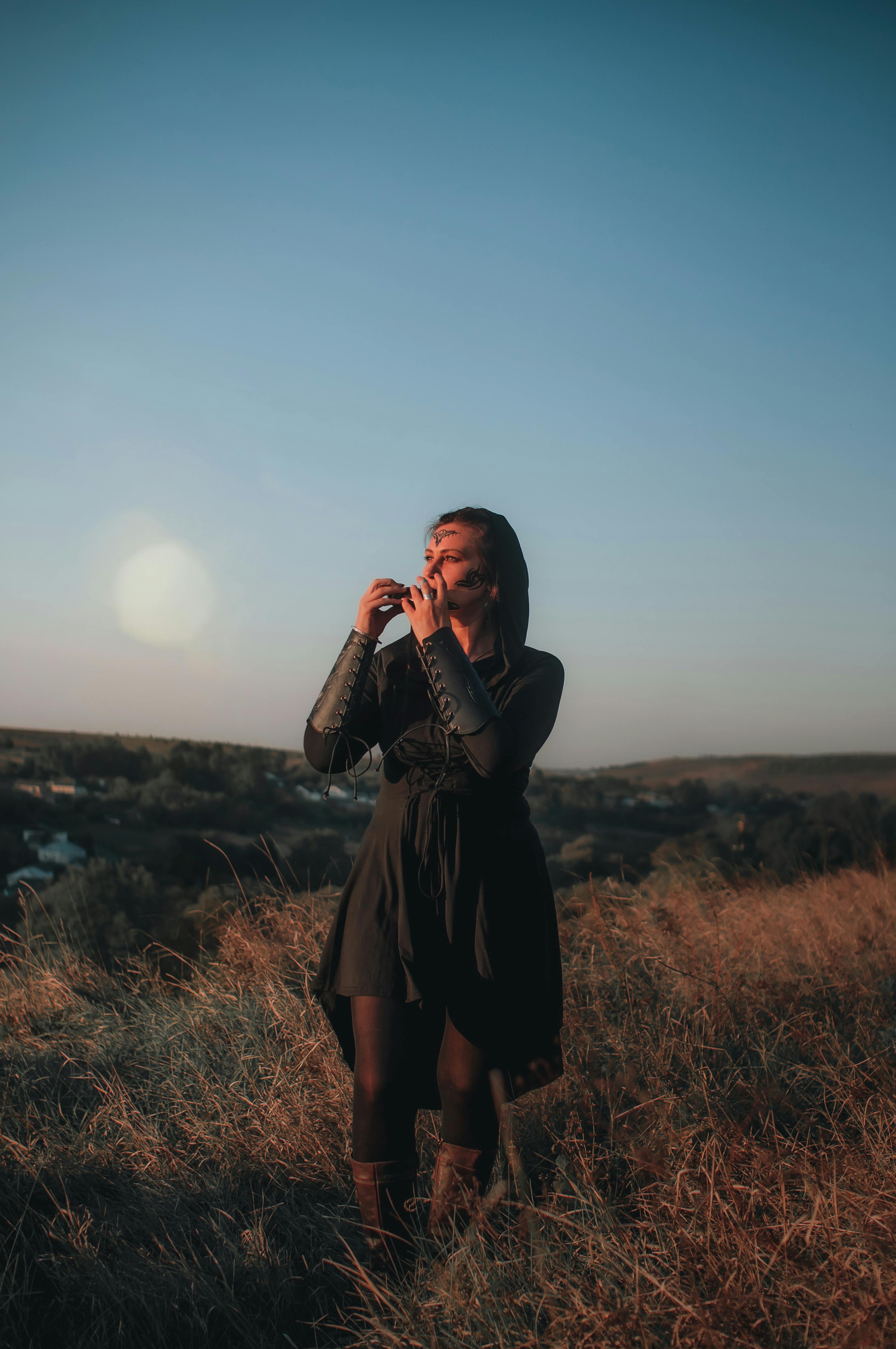Free A woman stands in a field at sunset, embracing the natural beauty around her. Stock Photo