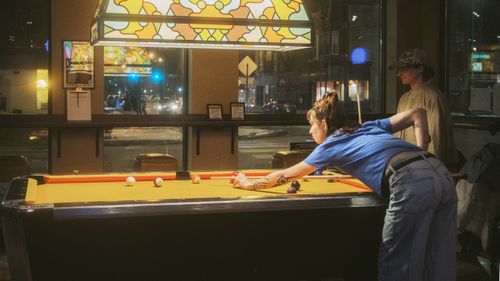 Free Two young adults enjoying a game of billiards in a warmly lit, cozy bar setting. Stock Photo