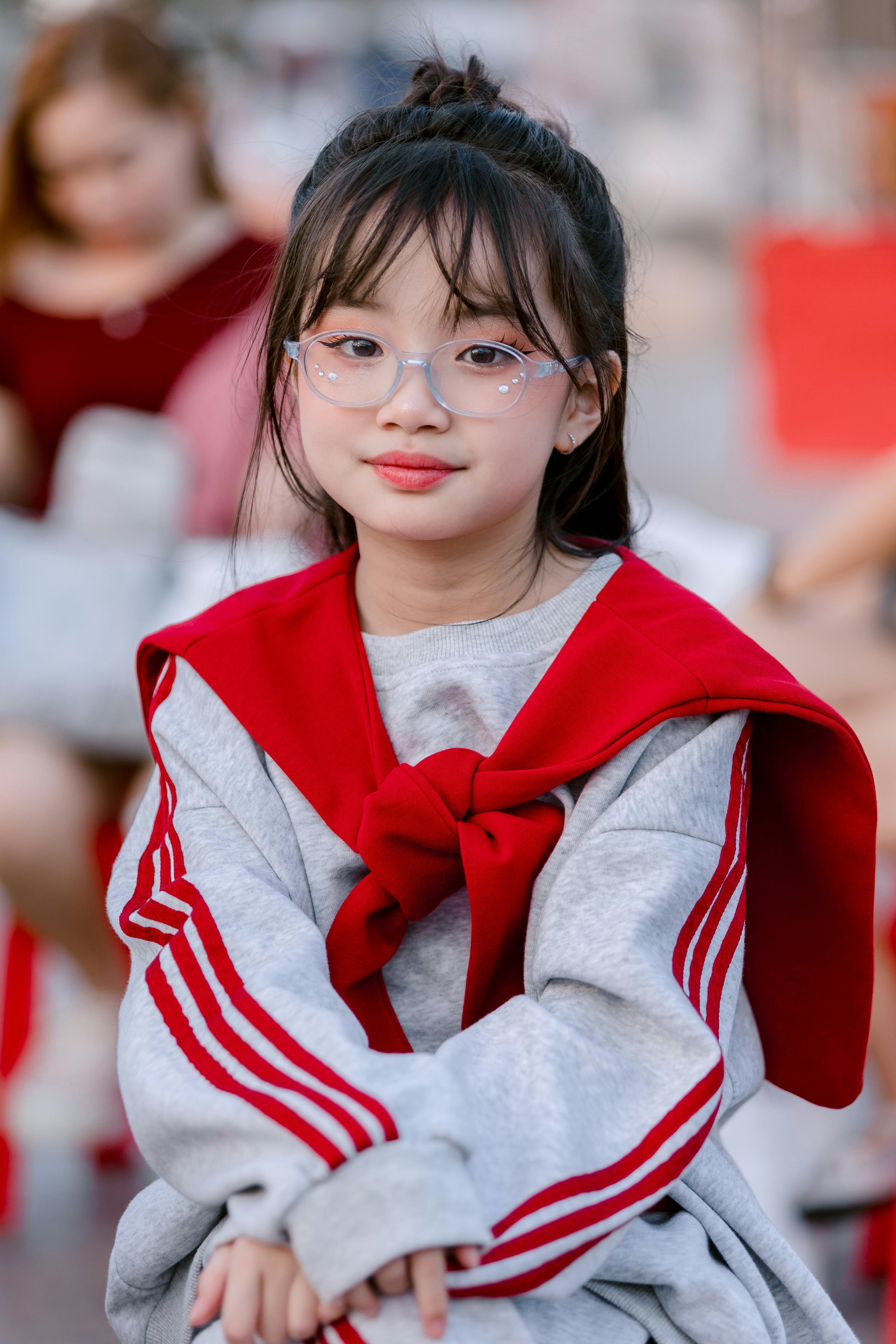 免费 一位戴着眼镜、身穿红灰色休闲装的迷人年轻女孩坐在户外。 素材图片