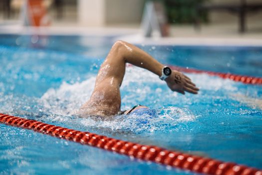 An athlete swims freestyle in an indoor pool, showcasing skill and endurance during a race.