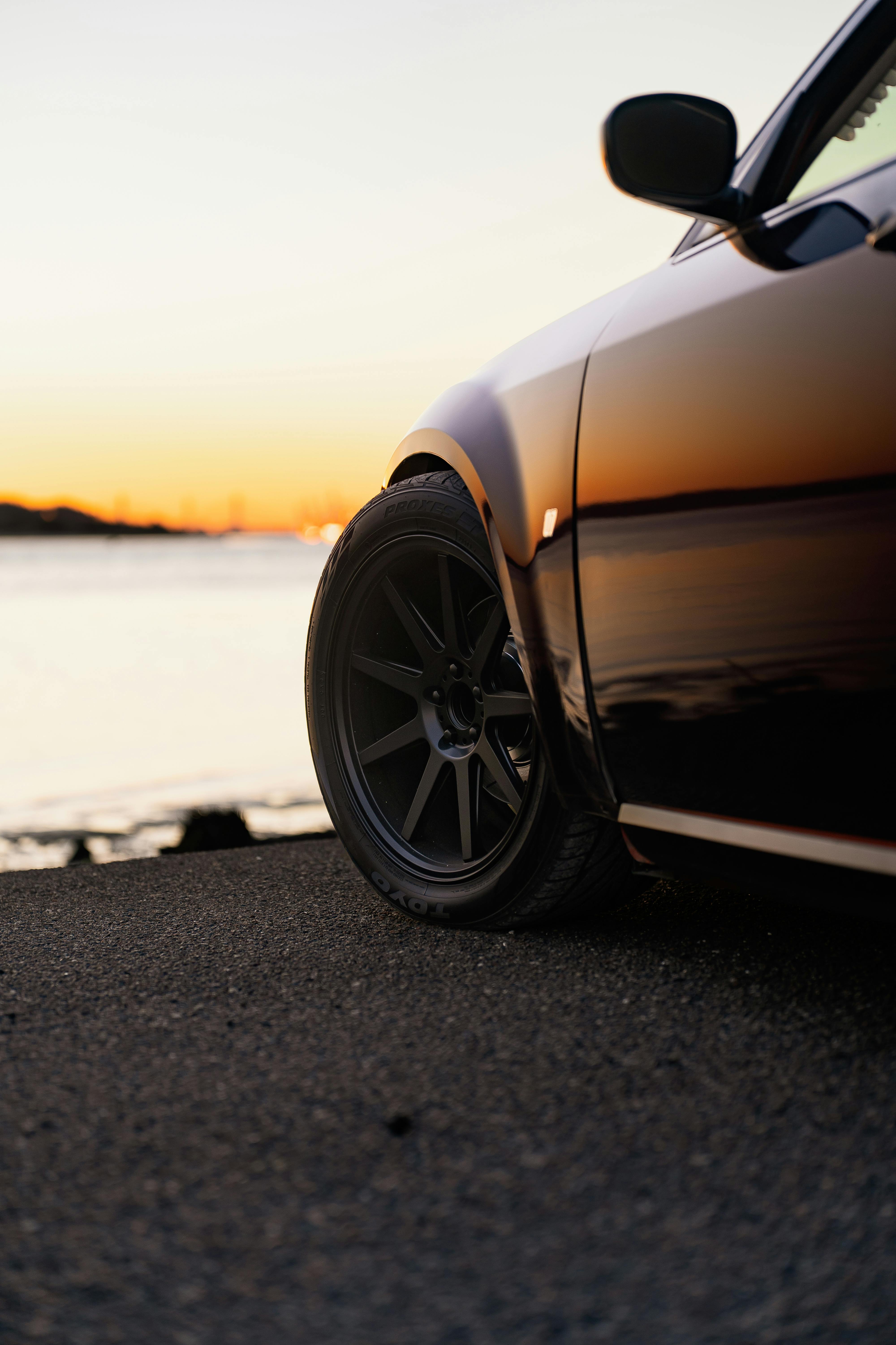 Zadarmo Elegantné moderné auto zaparkované pri vode s úžasným odrazom západu slnka na jeho hladine. Fotka z fotobanky