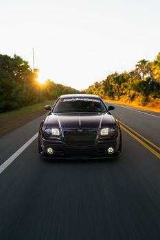 A sleek luxury car cruising on an open road with a beautiful sunset backdrop, perfect for automotive enthusiasts.