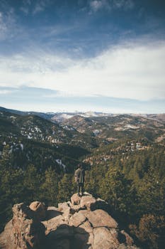 一位徒步旅行者站在悬崖边，欣赏着科罗拉多山脉和森林的景色