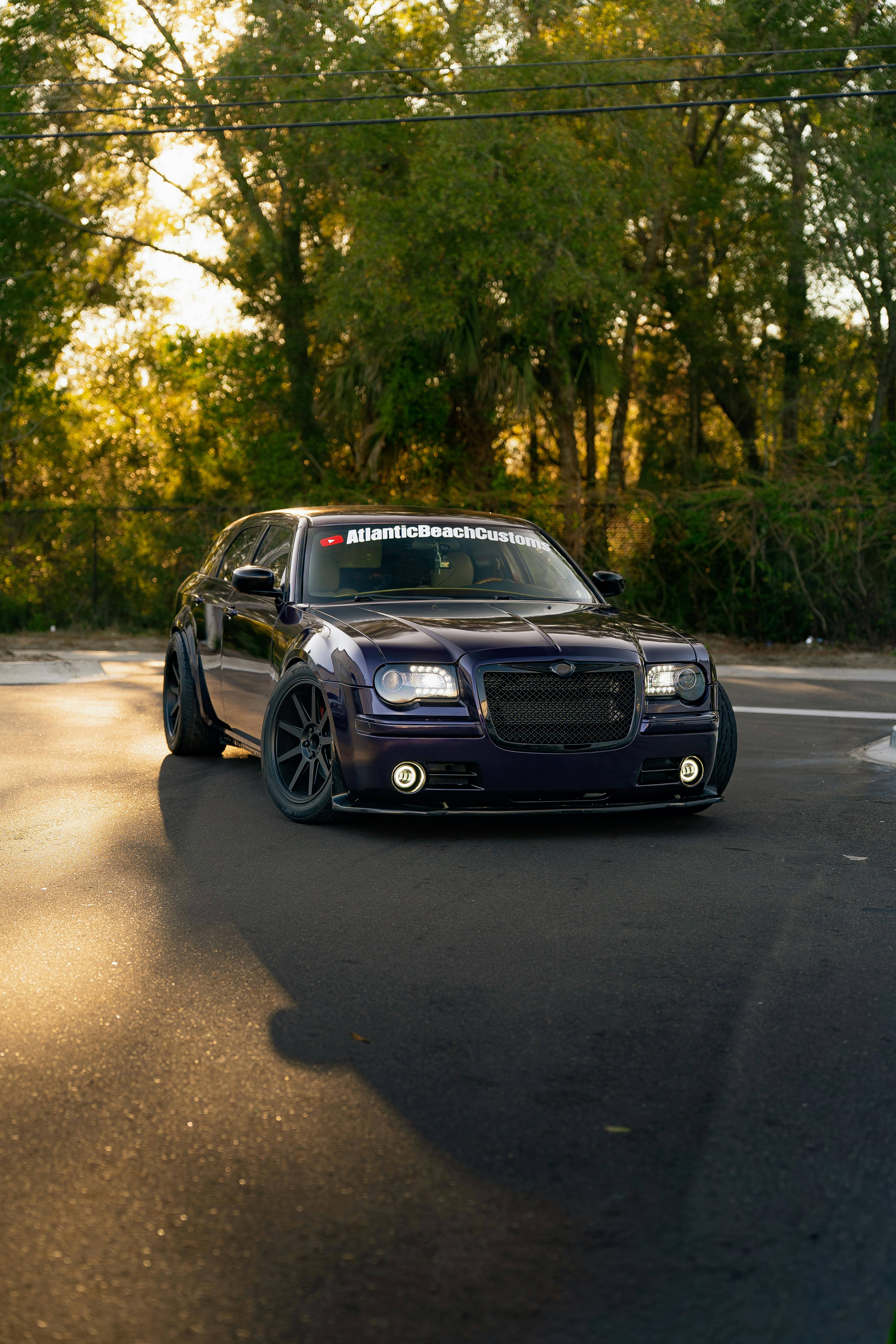 無料 改造された機能を備えた洗練された黒のカスタムカーが、日光が当たる道路に駐車されています。 写真素材