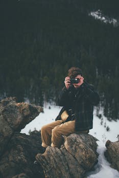 一名男子坐在岩石上，用相机拍摄自然风光