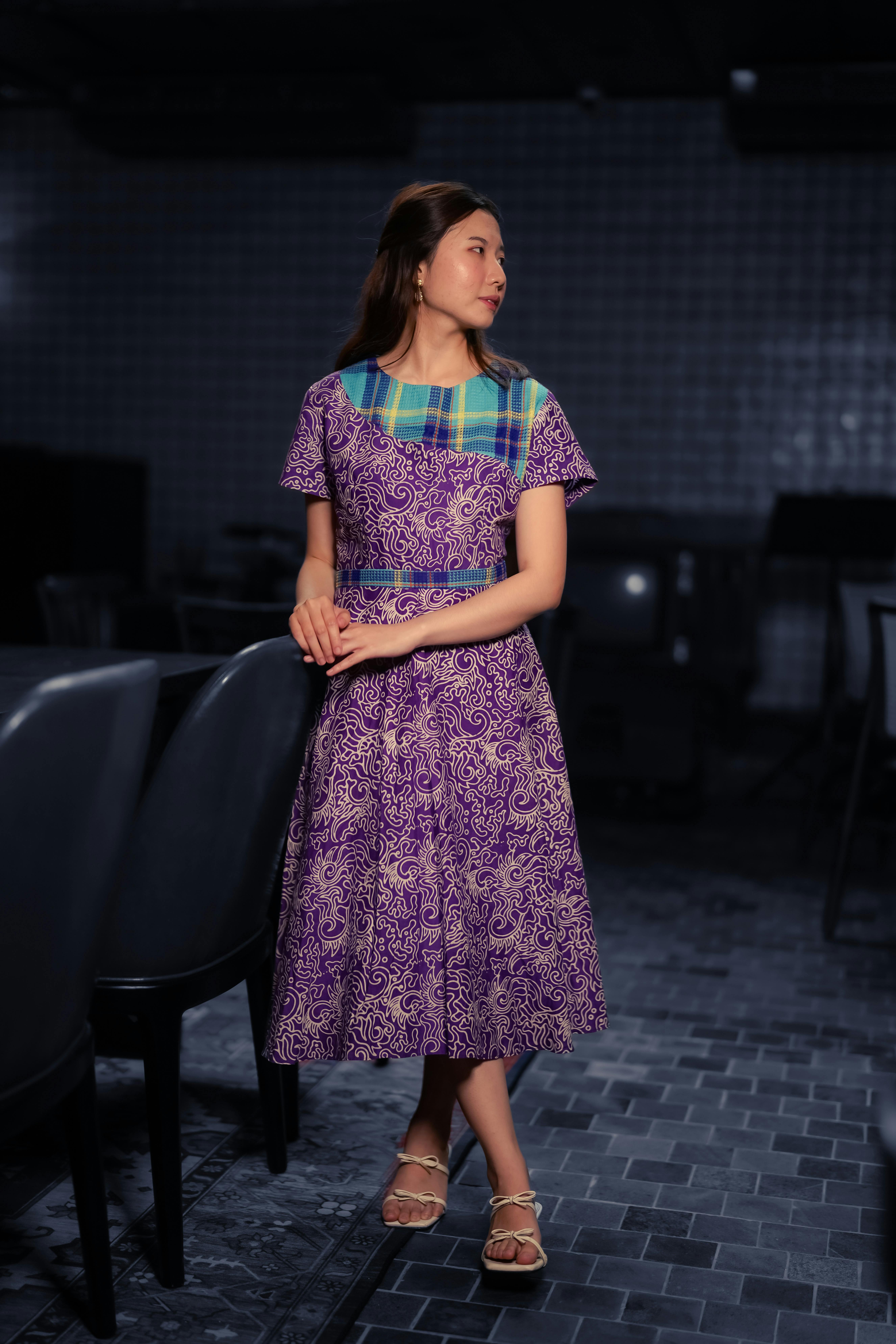 бесплатная В Джакарте элегантно одетая женщина стоит в современном помещении, демонстрируя традиционный наряд фиолетового цвета. Стоковое фото