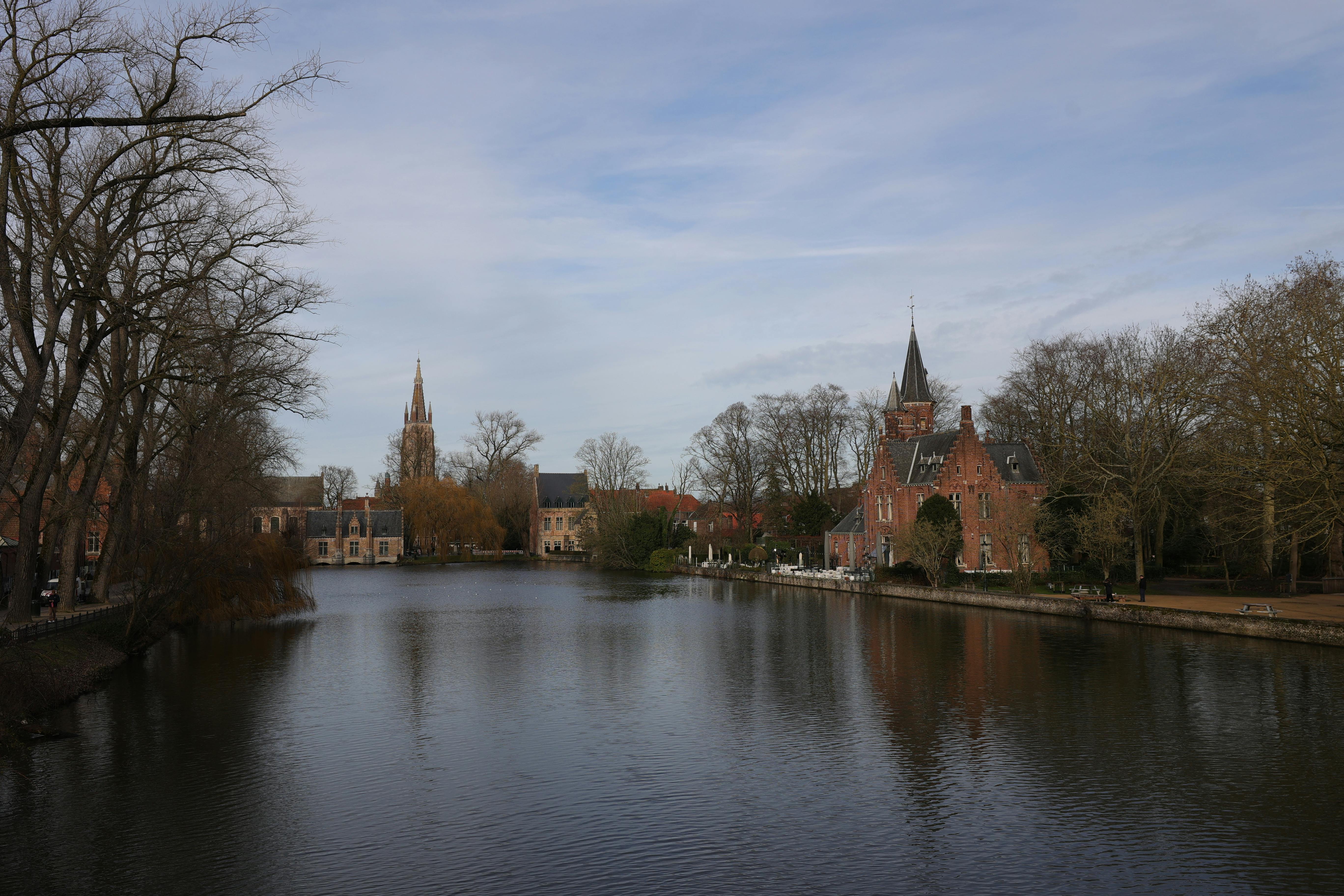 Gratis Opplev den fredelige skjønnheten til Brugges historiske kanal, omkranset av sjarmerende bygninger under en myk himmel. Arkivbilde