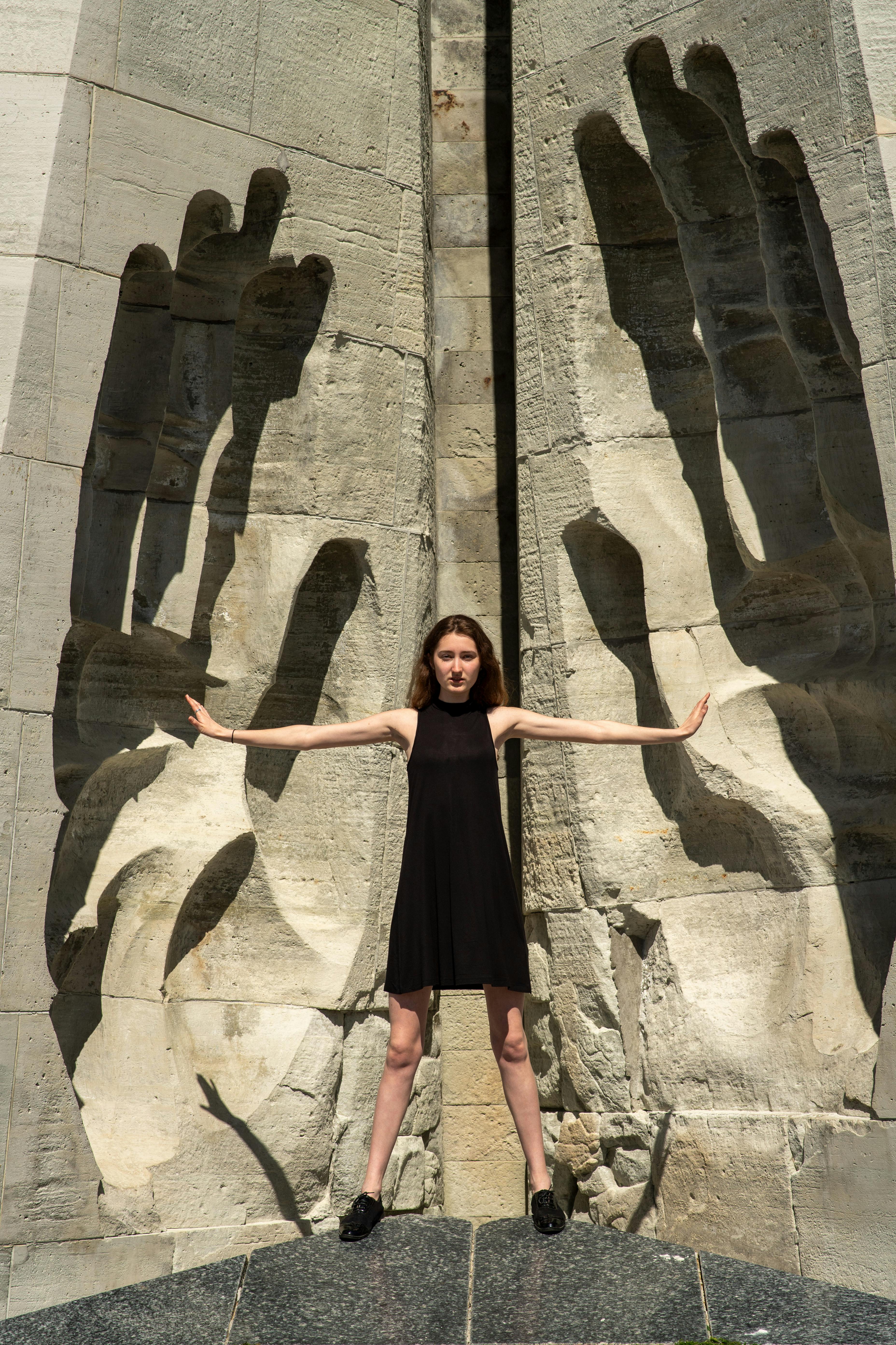 Gratis Seorang wanita muda berpose kreatif di depan sebuah patung batu besar di Tallinn, Estonia. Foto Stok
