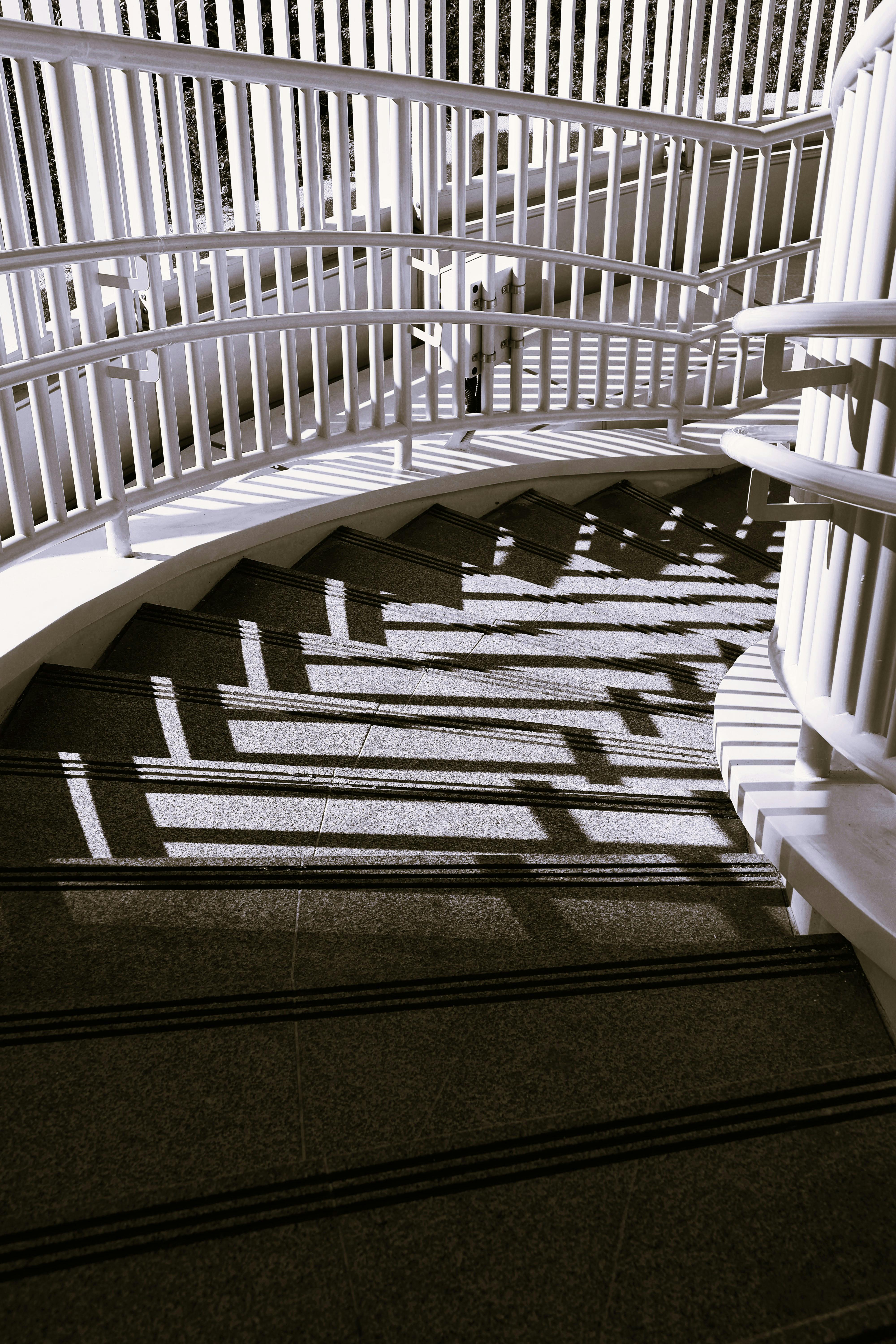 Gratuit Vue saisissante d'un escalier courbe, les ombres complexes projetées par la rampe offrant un spectacle magnifique. Photos