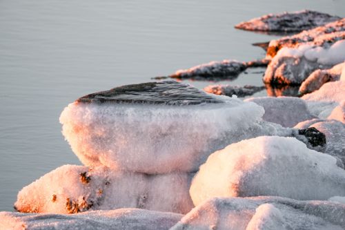 Free Icy rocks by the shore illuminated by a warm sunset glow, creating a serene winter scene. Stock Photo