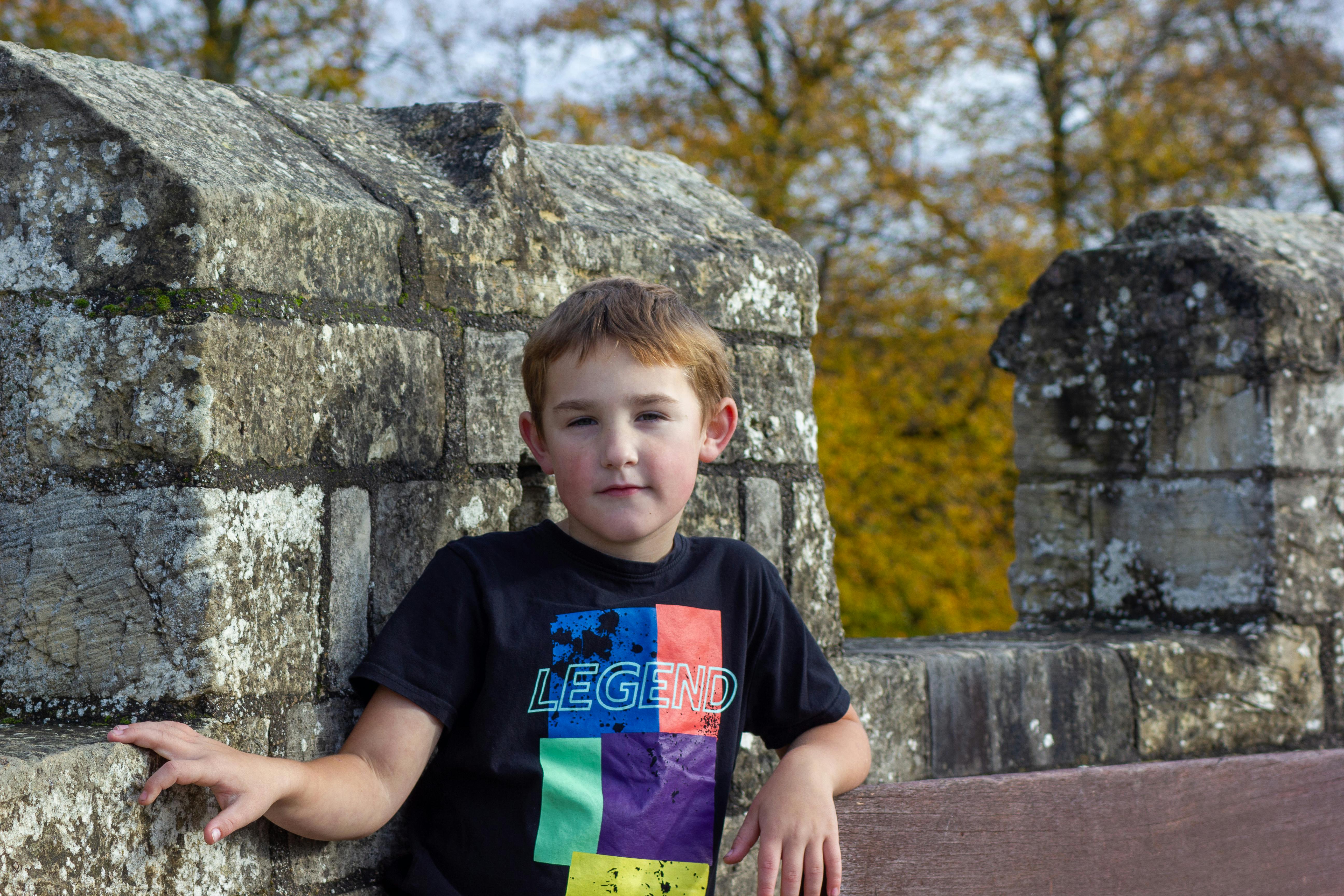 бесплатная Ребенок в яркой рубашке улыбается на фоне древней каменной стены осенью. Стоковое фото