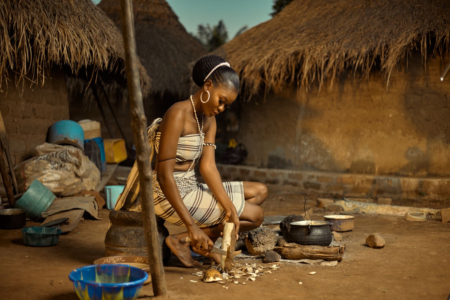 Woman prepares food using traditional methods in an African village setting.