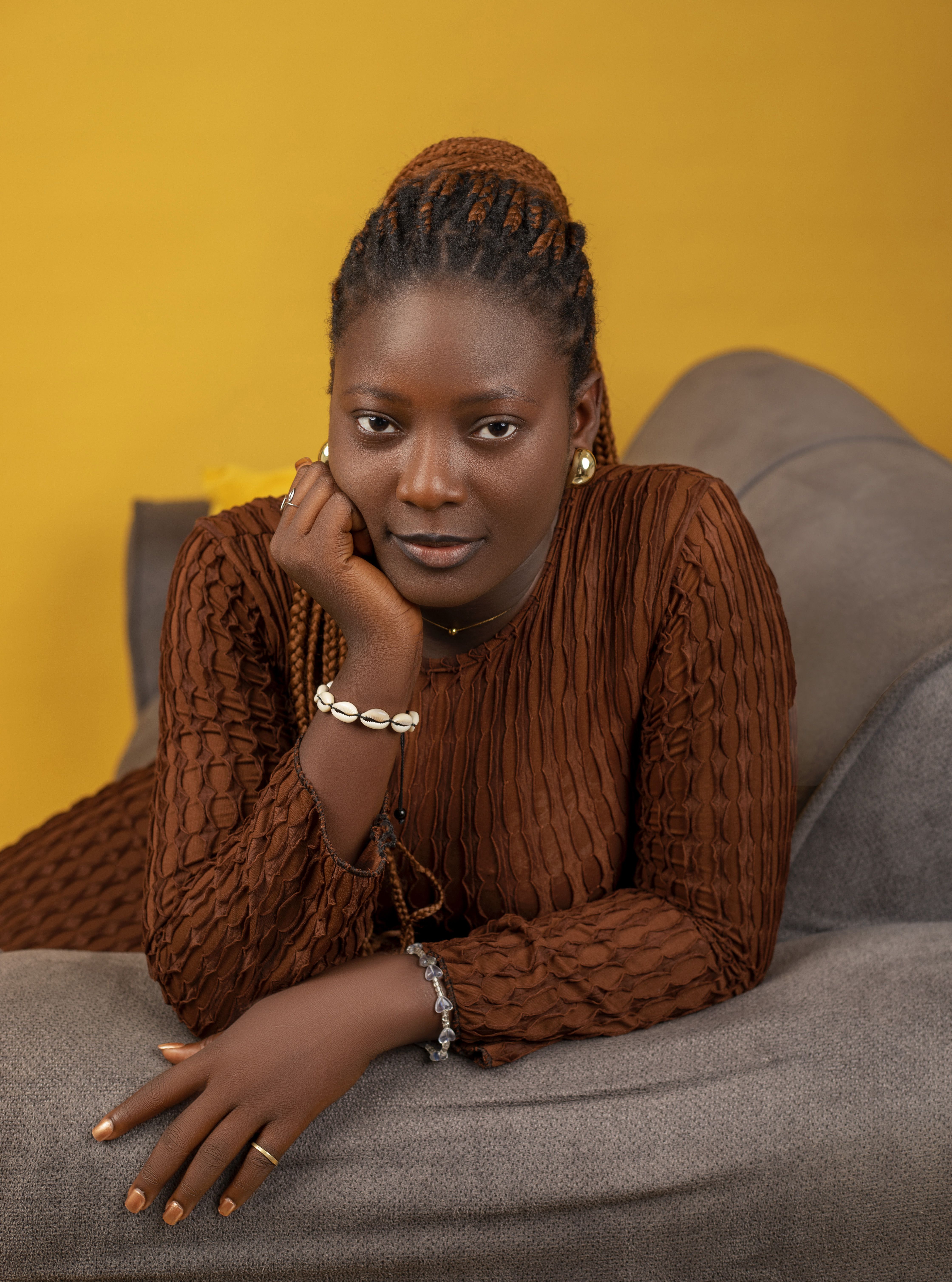 Stylish woman posing gracefully on a sofa with a warm yellow background.