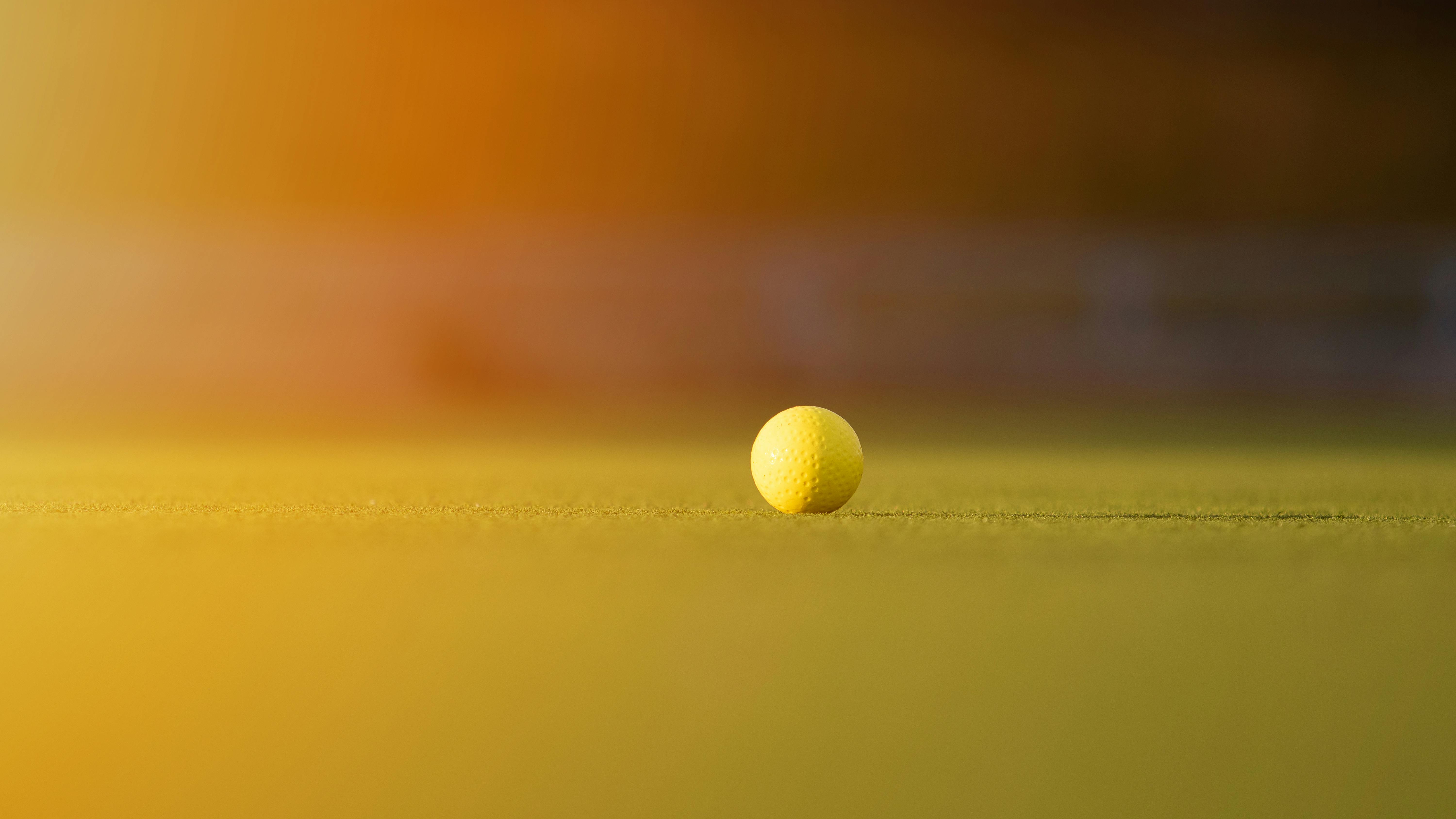 Close-up of a yellow golf ball on a sunlit grassy field, capturing a serene and vibrant outdoor setting.