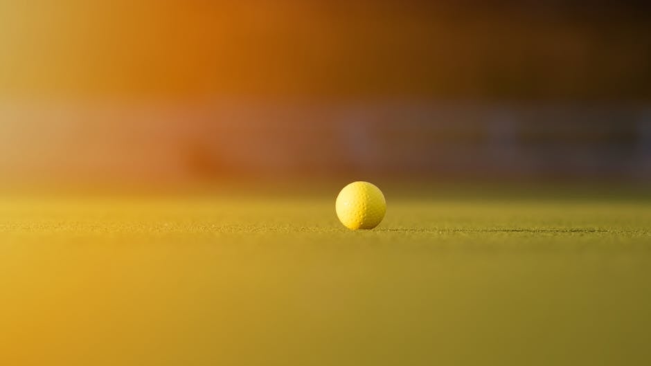 Close-up of a yellow golf ball on a sunlit grassy field, capturing a serene and vibrant outdoor setting.