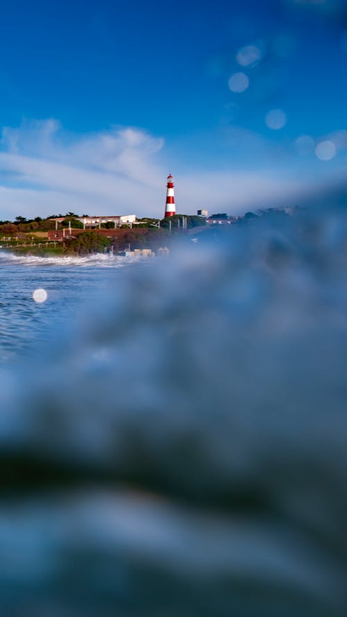 White and Red Lighthouse Near Body of Water Under White Clouds and Blue Sky