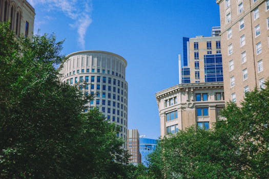 Urban skyline with modern and classic architecture, framed by lush greenery and a clear blue sky.