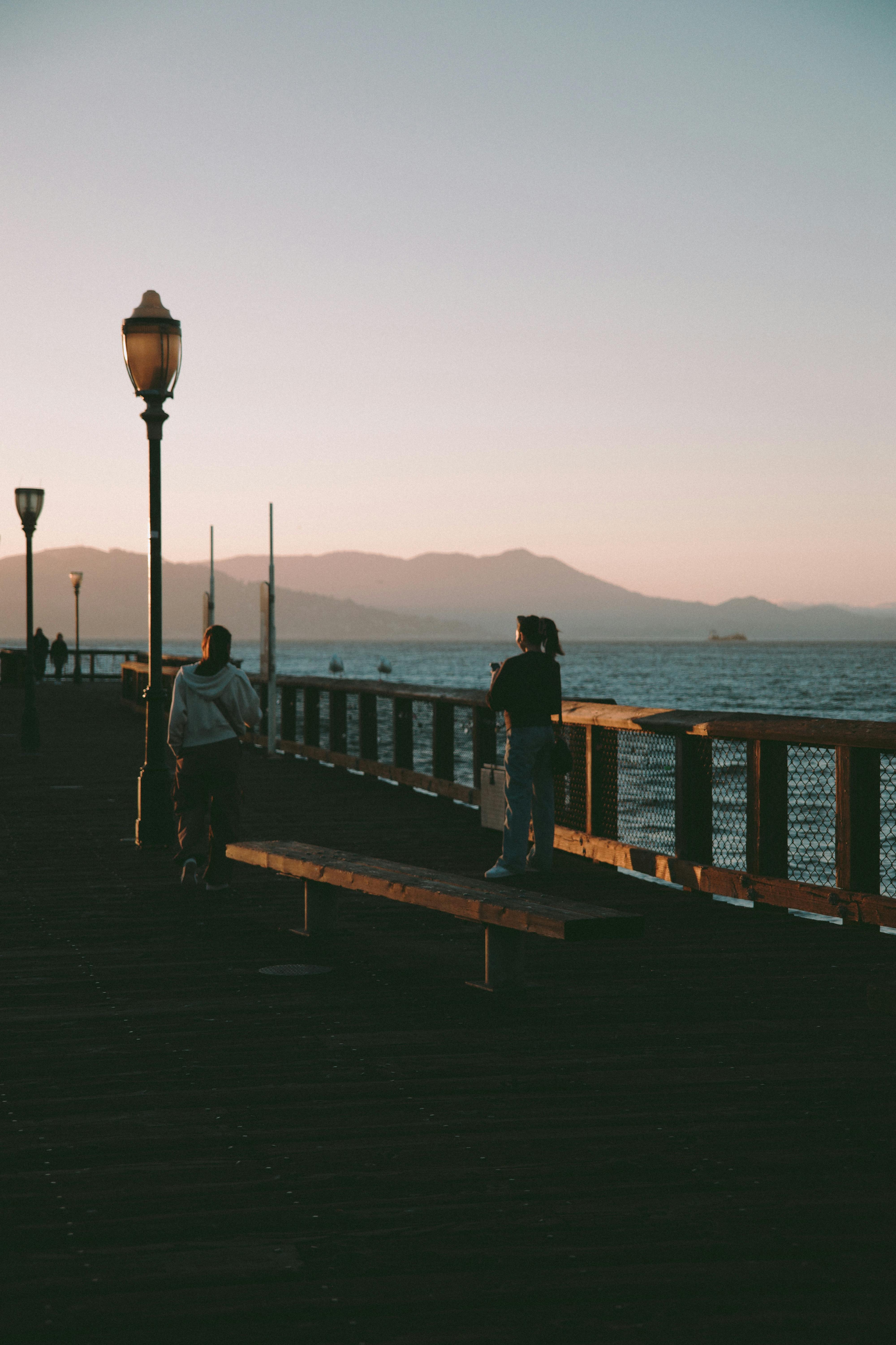 免费 夕阳西下，两人走在码头上，远处是连绵的群山。 素材图片