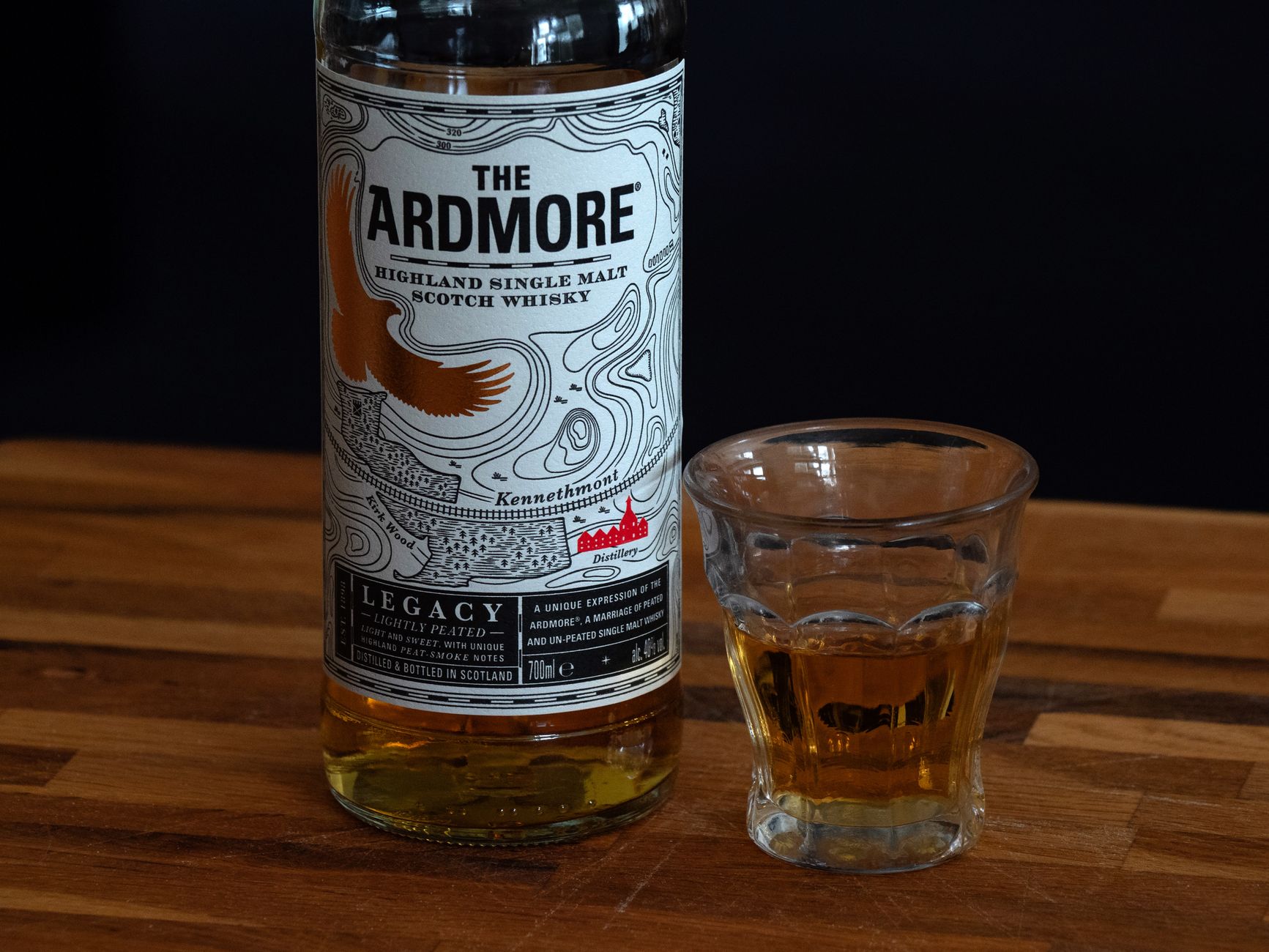A glass of peaty Islay whisky with dark amber liquid catching light against a moody background.