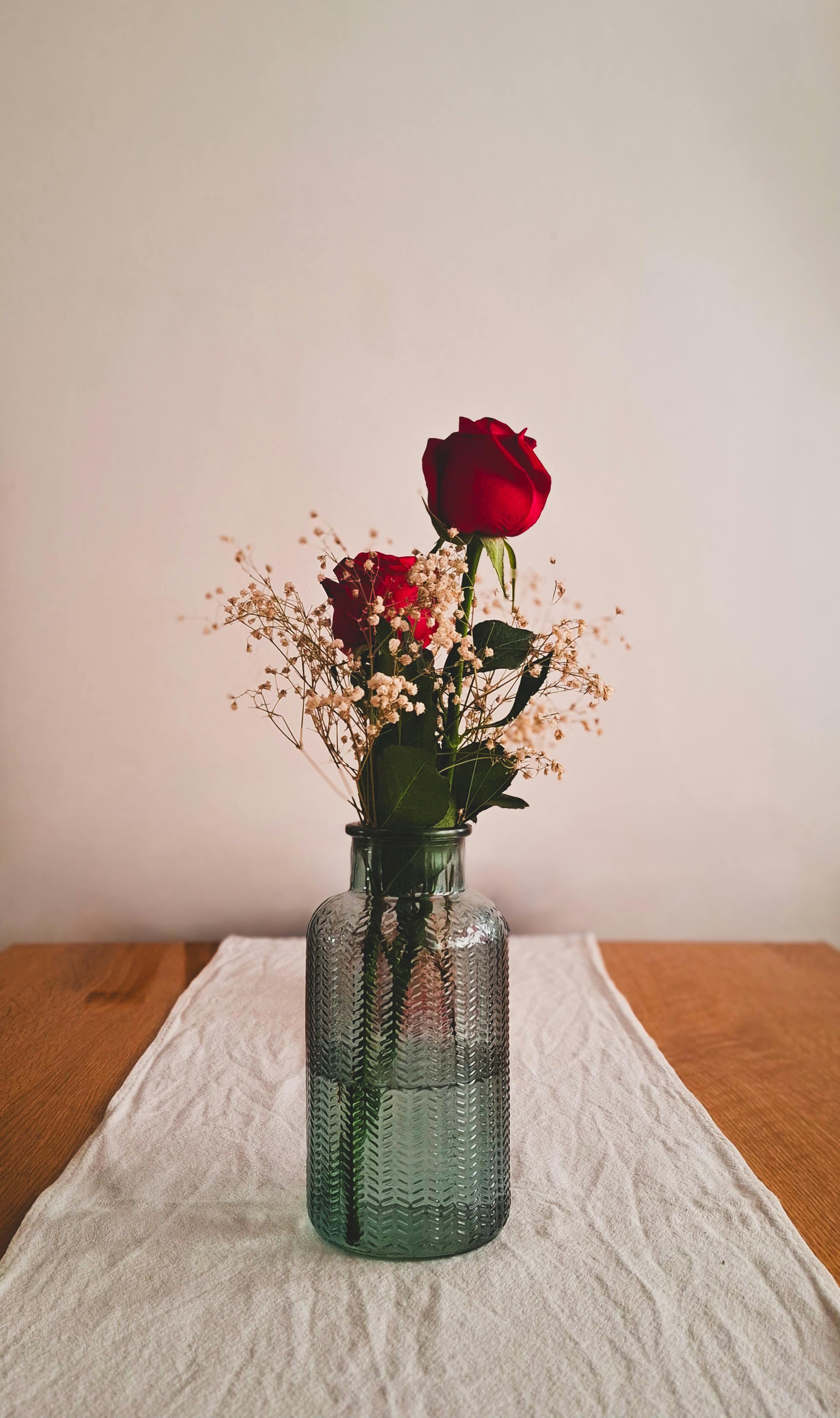 Gratis Arreglo estético de rosas rojas y flores blancas en un jarrón de vidrio texturizado sobre una mesa de madera. Foto de stock