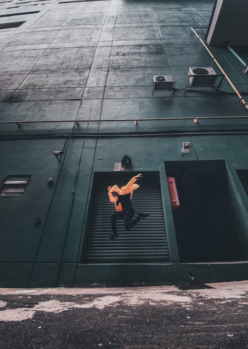 бесплатная Мужчина в оранжевой куртке и черных штанах прыгает Стоковое фото