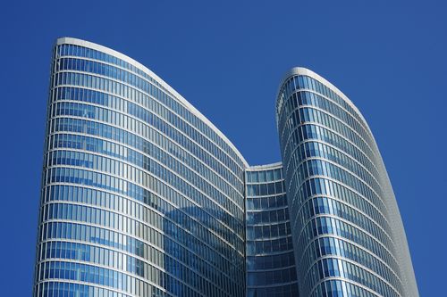 Free Architectural view of a sleek, modern skyscraper in Dubai with reflective glass windows against a vibrant blue sky. Stock Photo