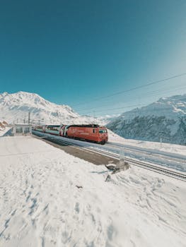 Red train traveling through the snowy Swiss Alps on a clear winter day.