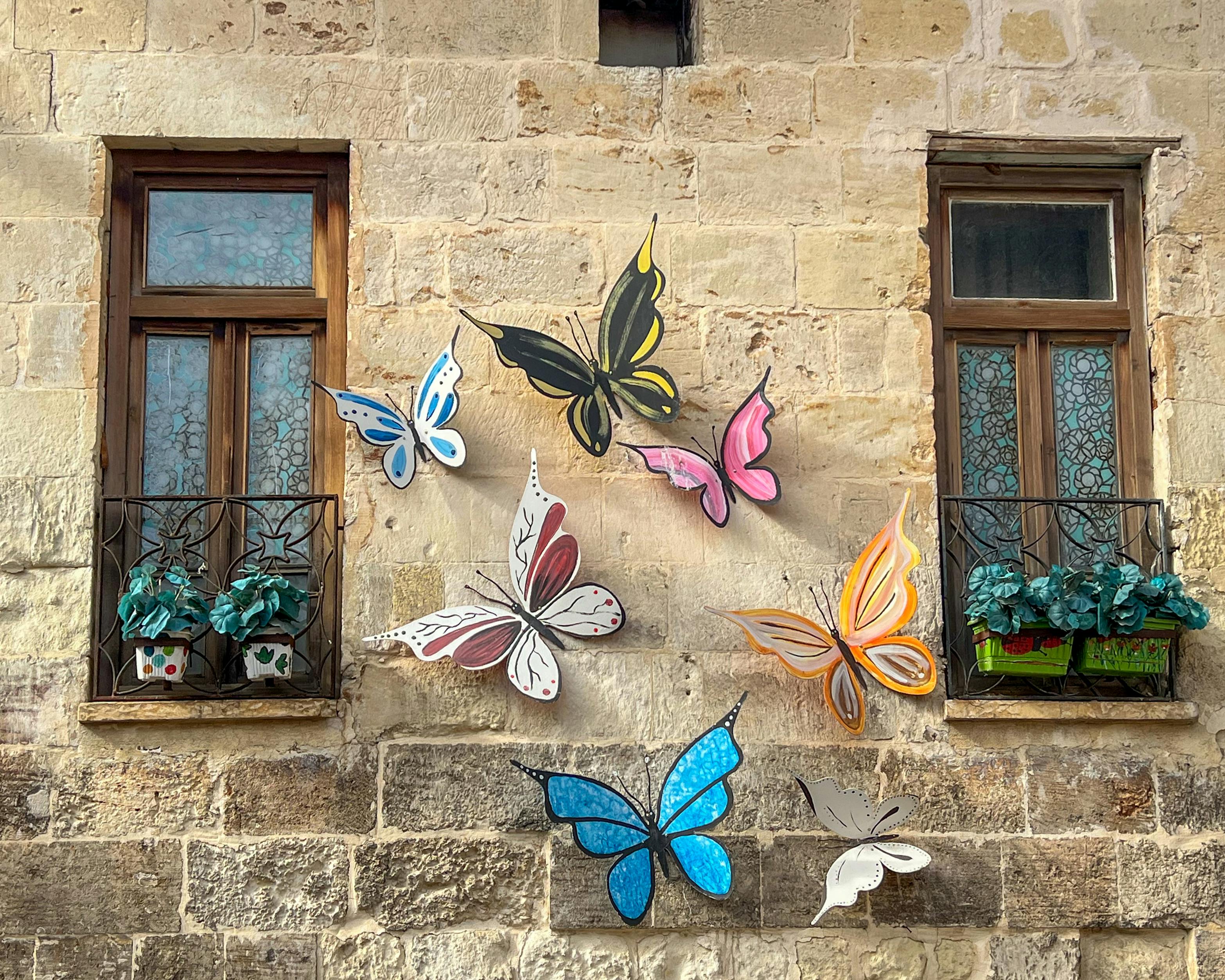 Gratis Snuriøse sommerfugldekorasjoner lyser opp en rustikk steinvegg med vintagevinduer. Arkivbilde