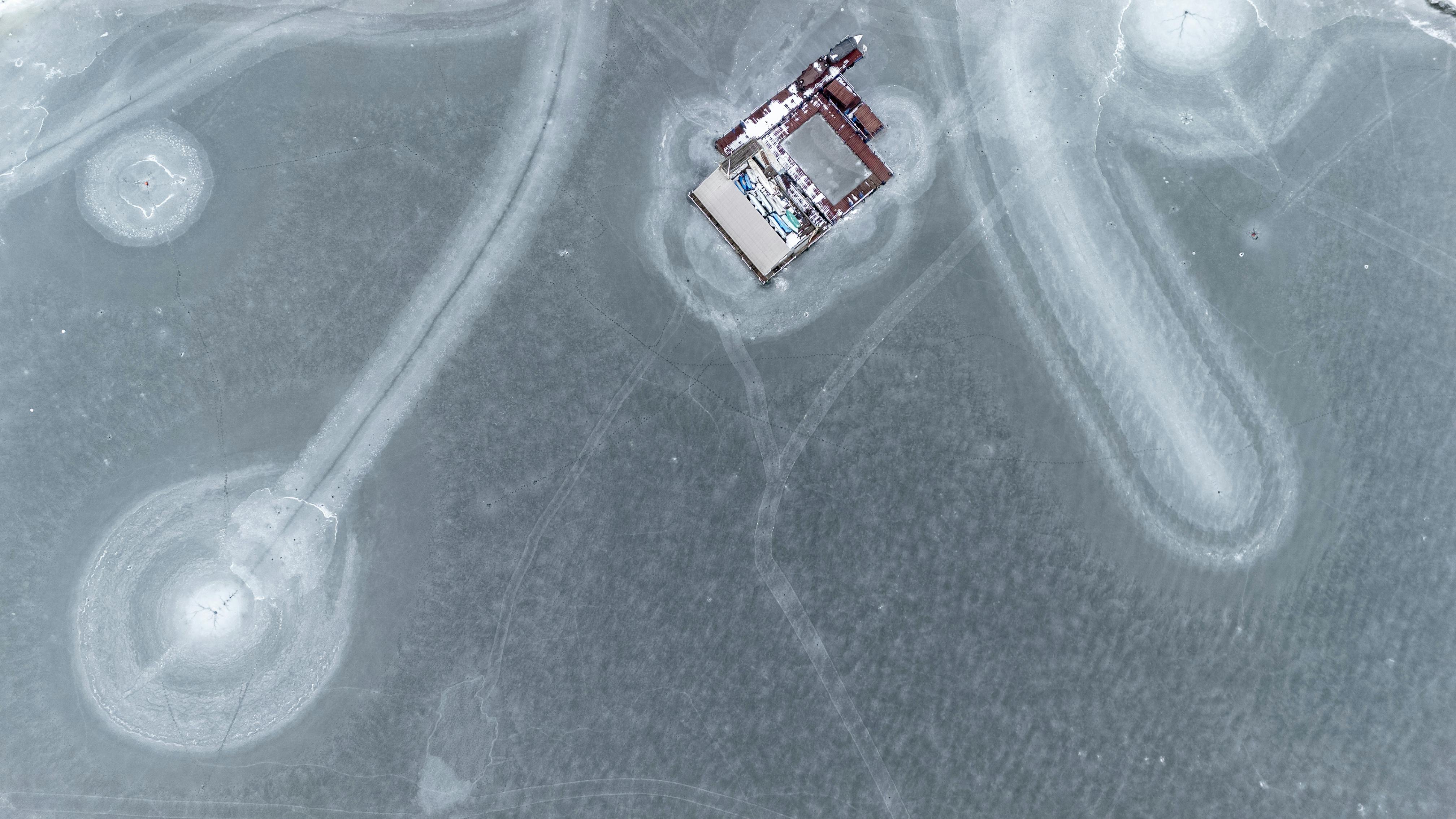 Ilmainen Ilmakuva lumen peittämästä kuviollisesta ja rakennuksista koostuvasta jäätyneestä järvestä. Kuvapankkikuva