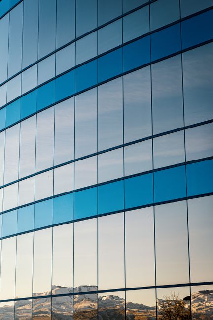 Sleek glass facade reflecting surrounding landscape, showcasing modern architecture.