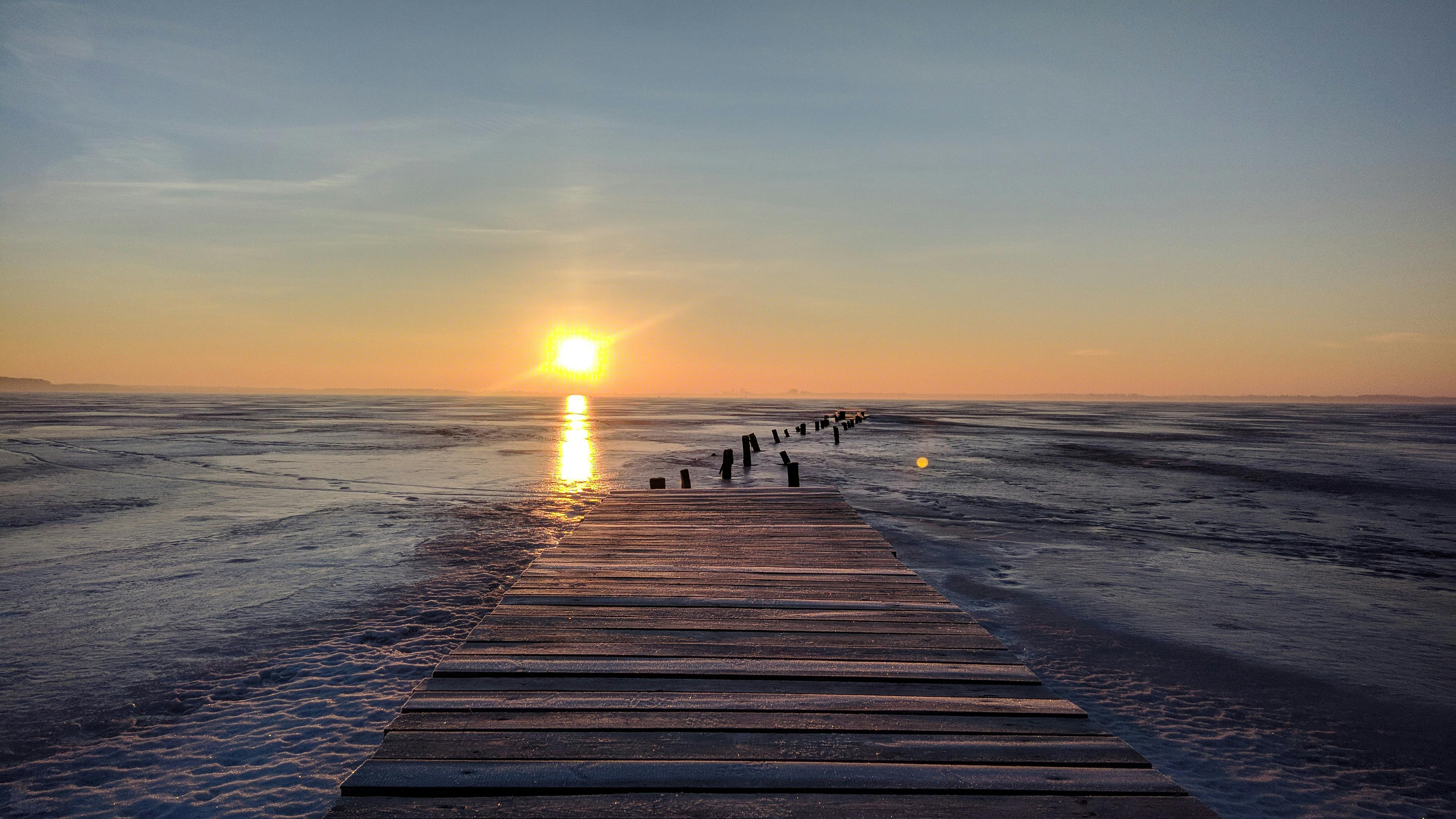 免费 夕阳西下，映照着冰封的湖面，远处延伸着一座木制码头。 素材图片