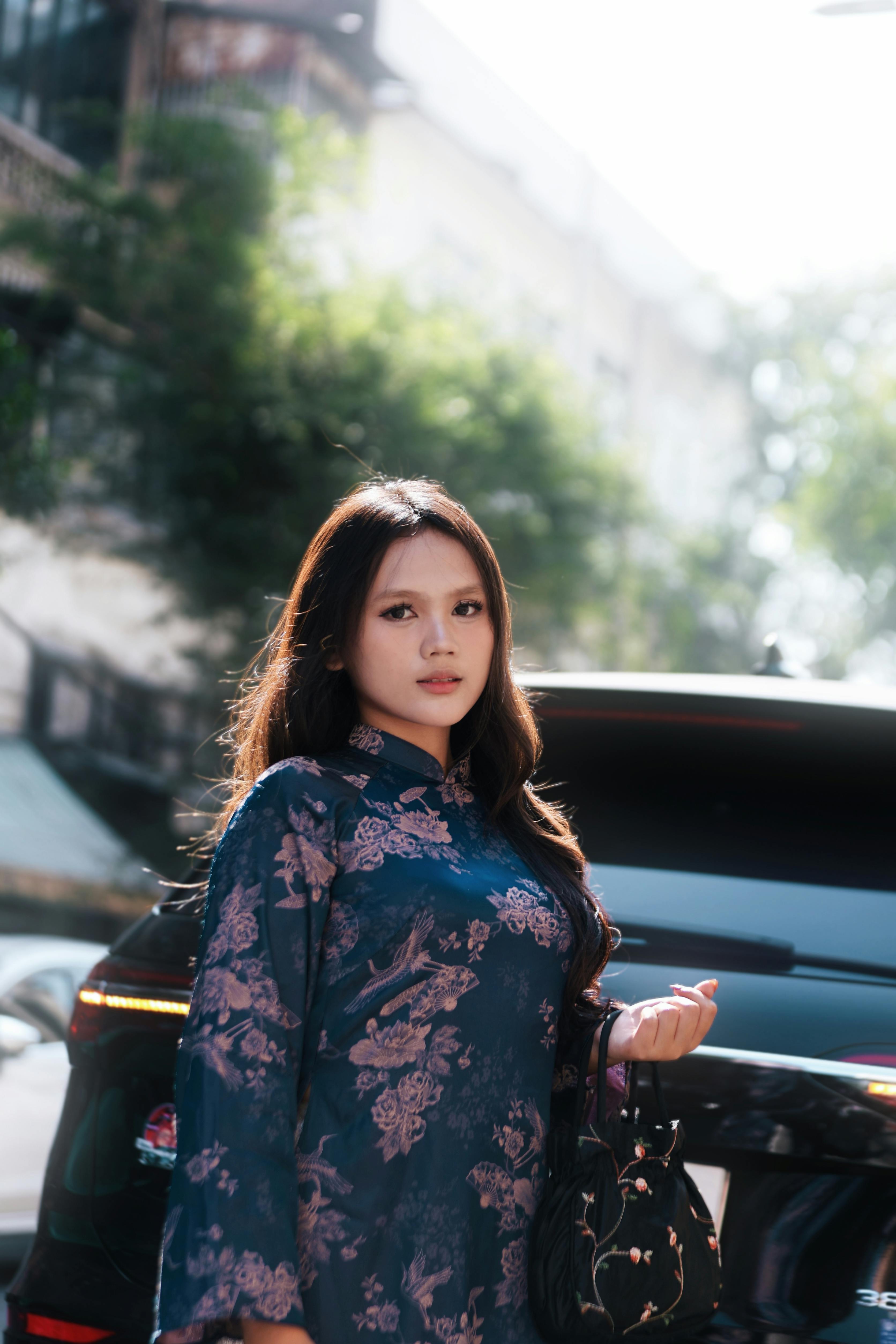 gratis Een jonge vrouw in een jurk met een patroon staat buiten bij een auto en straalt zelfvertrouwen uit in het zonlicht. Stockfoto