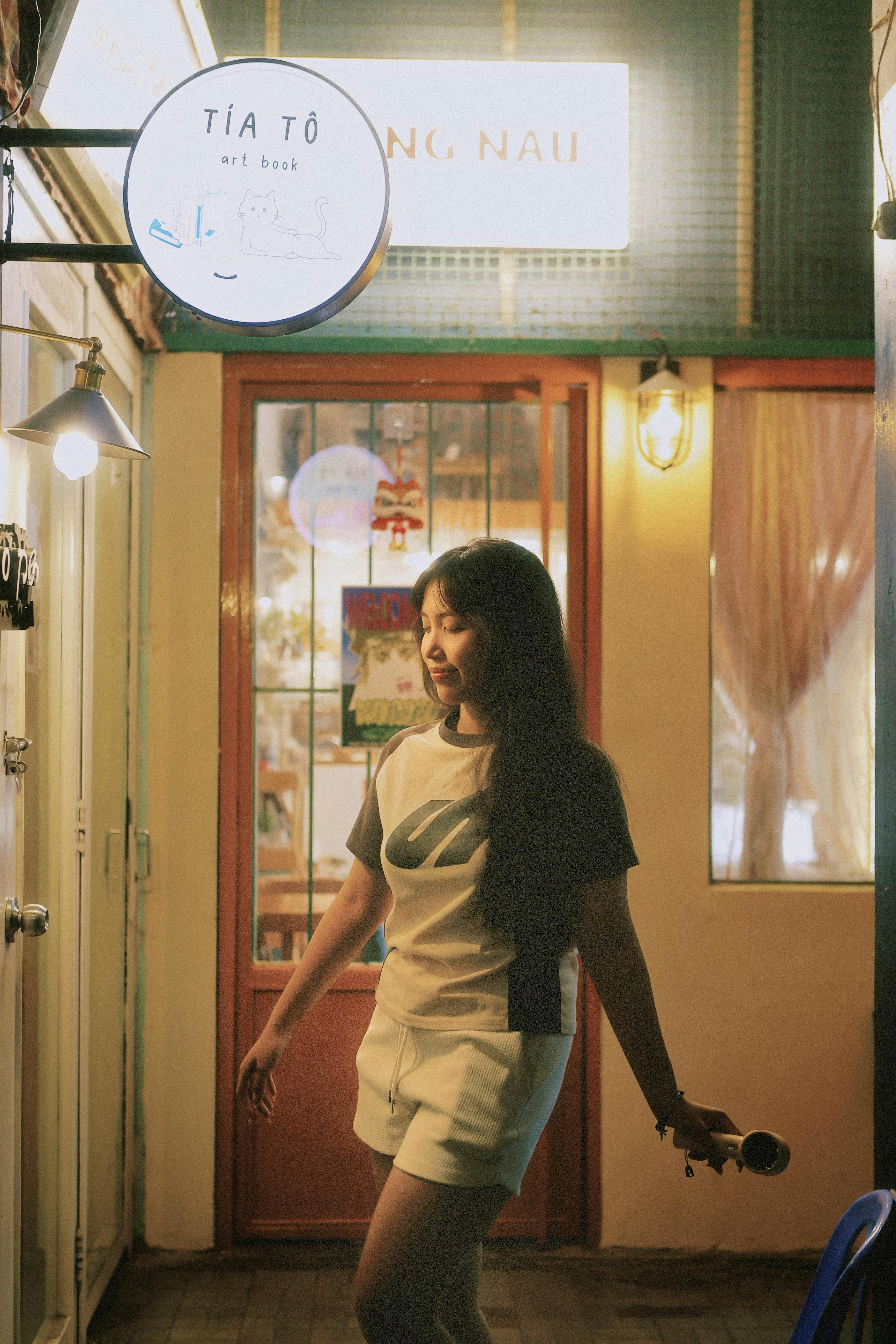 Miễn phí Một người phụ nữ tận hưởng buổi tối yên tĩnh bên ngoài một quán cà phê nghệ thuật được chiếu sáng ấm áp, toát lên một bầu không khí thư thái. Ảnh lưu trữ