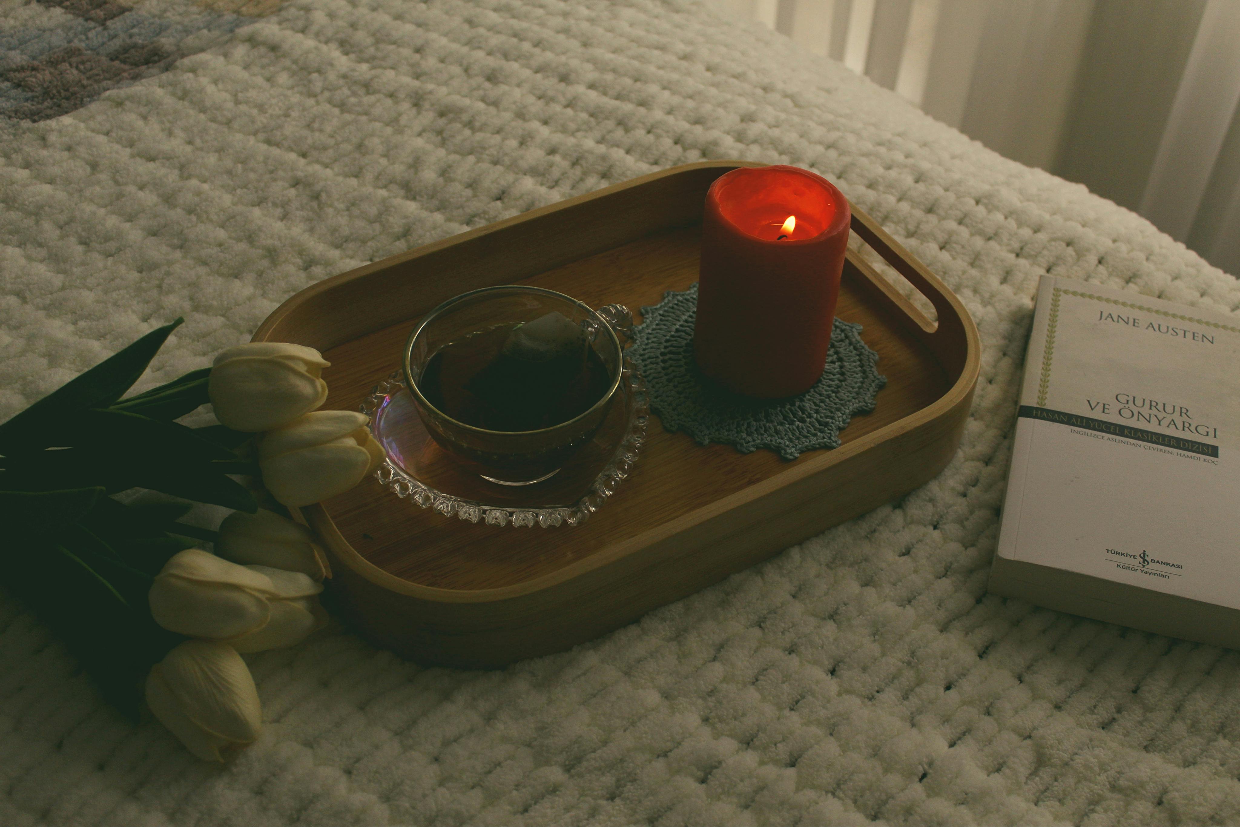 Kostenlos Eine beruhigende Szene am Bett mit einer brennenden Kerze, Tee und einem Buch für eine perfekte, gemütliche Atmosphäre. Stock-Foto