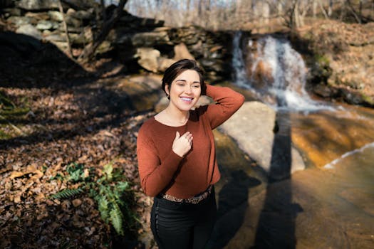一名年轻女子穿着休闲装，在森林瀑布附近微笑着摆姿势
