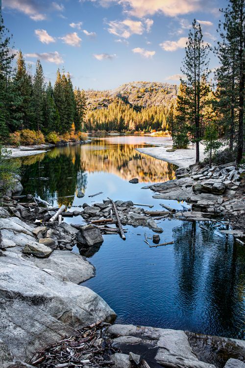 Free Peaceful lake surrounded by pine trees and rocky landscape, reflecting a vibrant sunset. Stock Photo