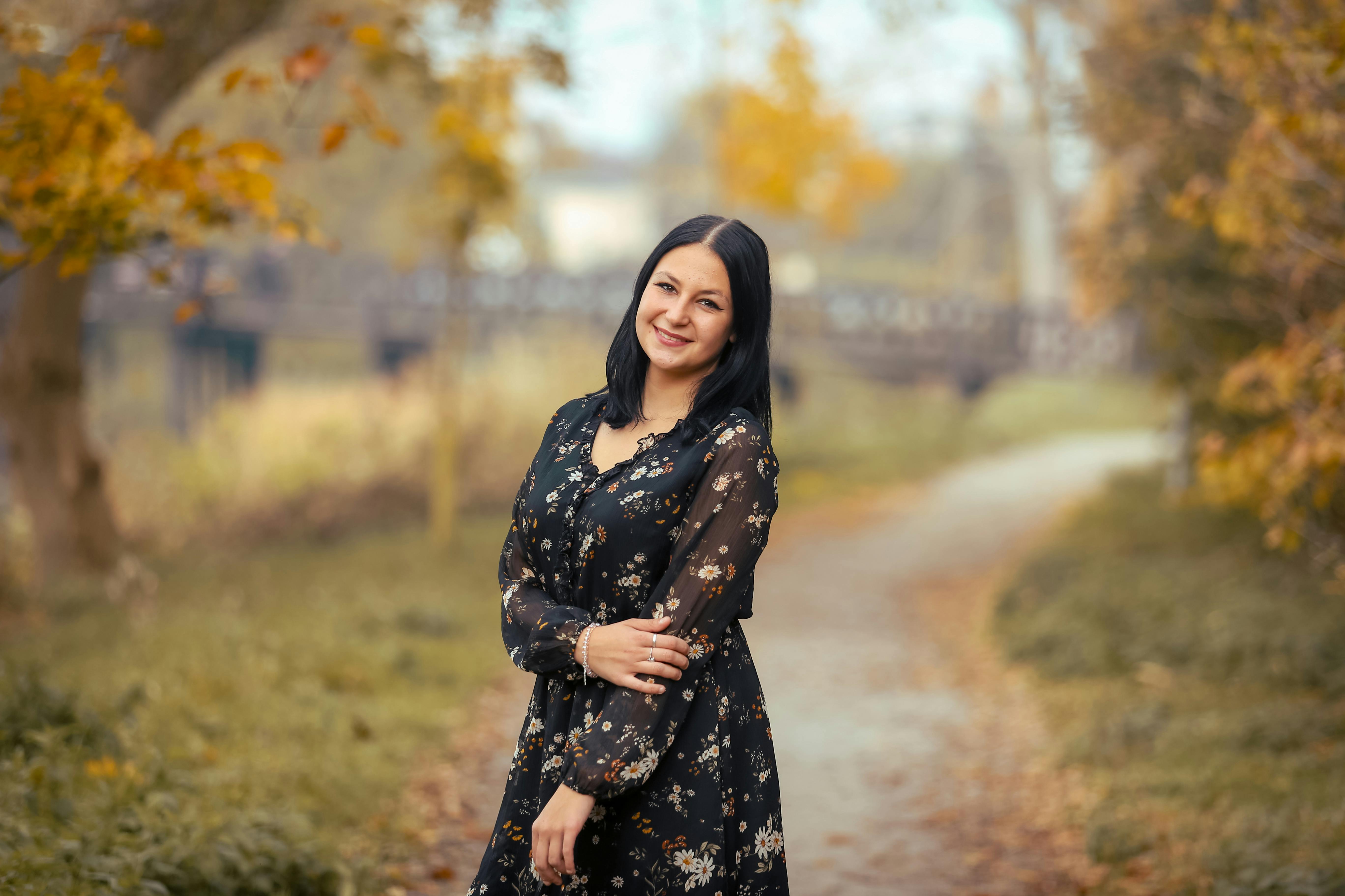 Δωρεάν Μια γυναίκα χαμογελάει και ποζάρει σε ένα ήσυχο φθινοπωρινό πάρκο περιτριγυρισμένο από φθινοπωρινό φύλλωμα. Φωτογραφία από στοκ φωτογραφιών