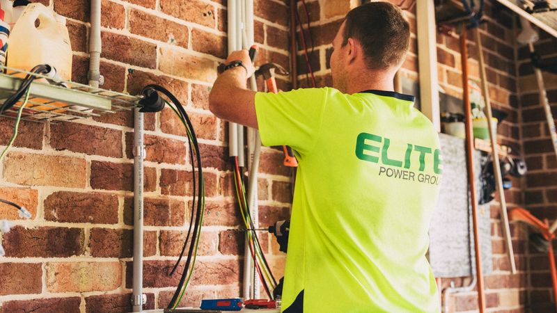 electrician installing a level 2 ev charger on a garage wall next to an electrical panel