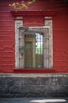 Textured red wall with a traditional barred window in Coyoacán, Mexico City.