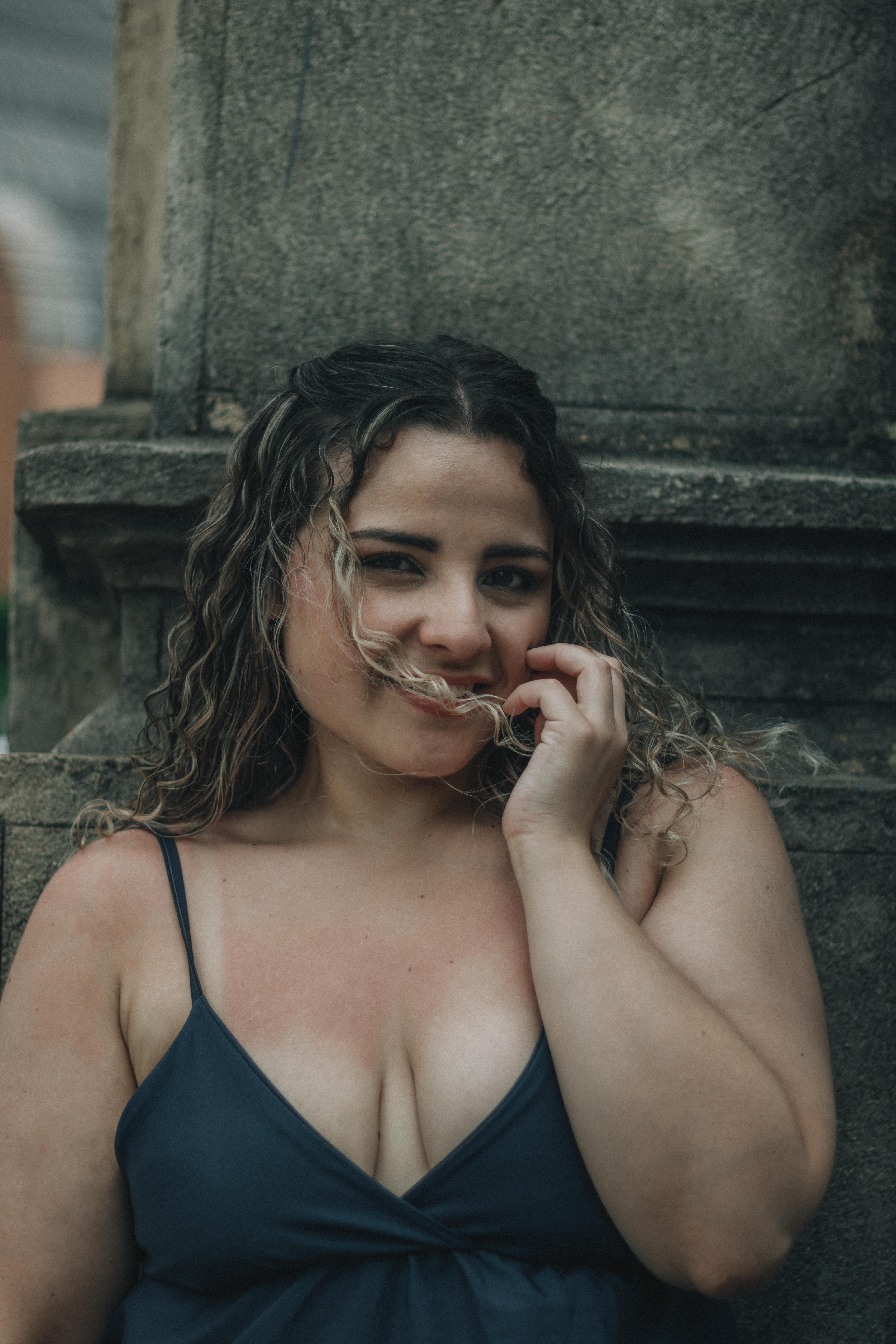 bezplatná Usmívající se žena s kudrnatými vlasy pózuje venku na kamenném pozadí. Základová fotografie