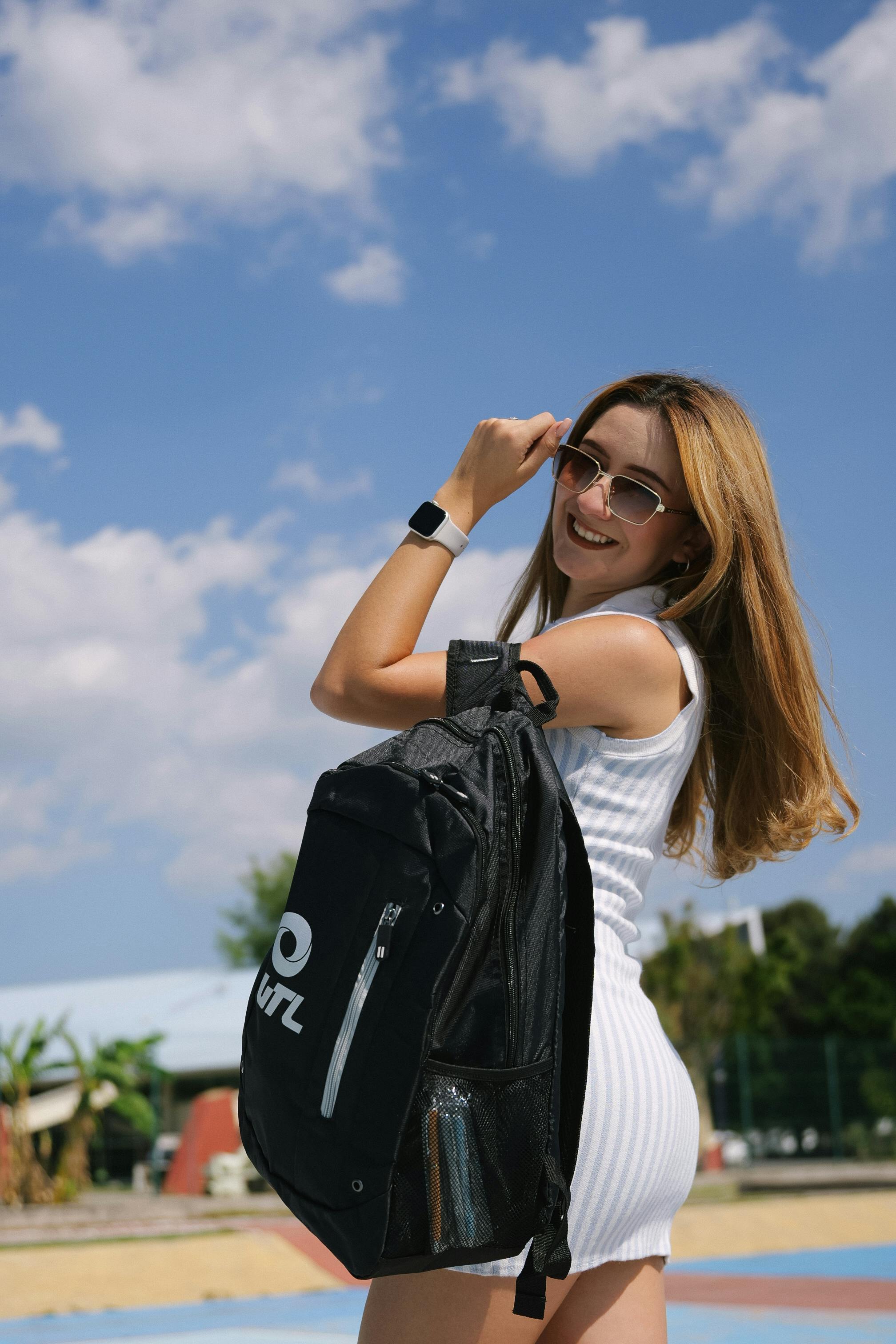 Gratis Donna elegante che posa con uno zaino in un ambiente soleggiato all'aperto, godendosi l'atmosfera estiva. Foto a disposizione