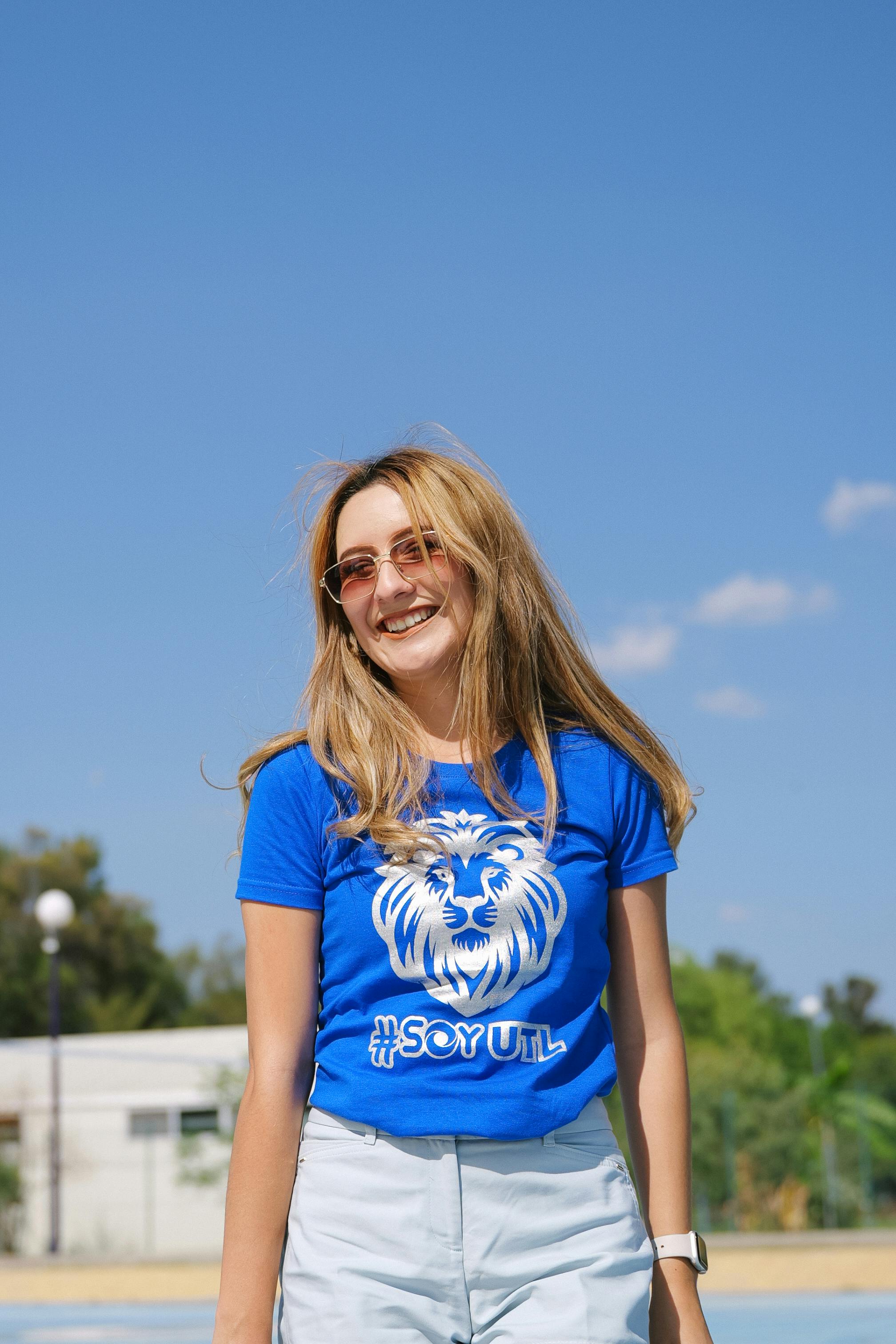 ingyenes Egy mosolygós nő napszemüvegben és kék pólóban élvezi a napsütéses napot a szabadban. Stockfotó