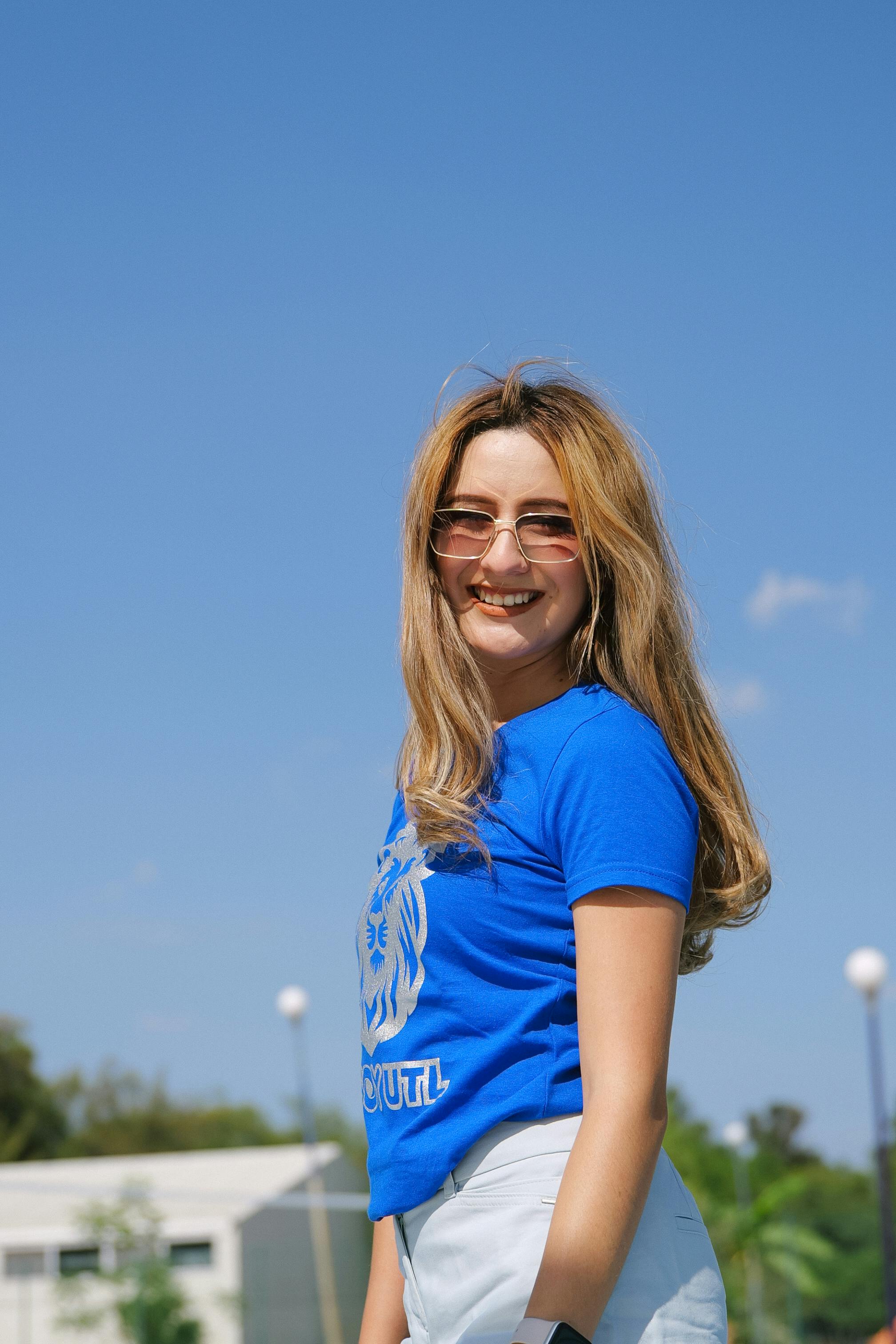 Gratis Donna felice che indossa occhiali da sole e una maglietta blu mentre si gode una giornata di sole all'aperto. Foto a disposizione