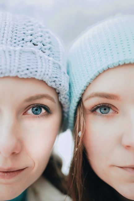 Two women in winter attire with knitted beanies, showcasing a close-up portrait highlighting beautiful eyes.