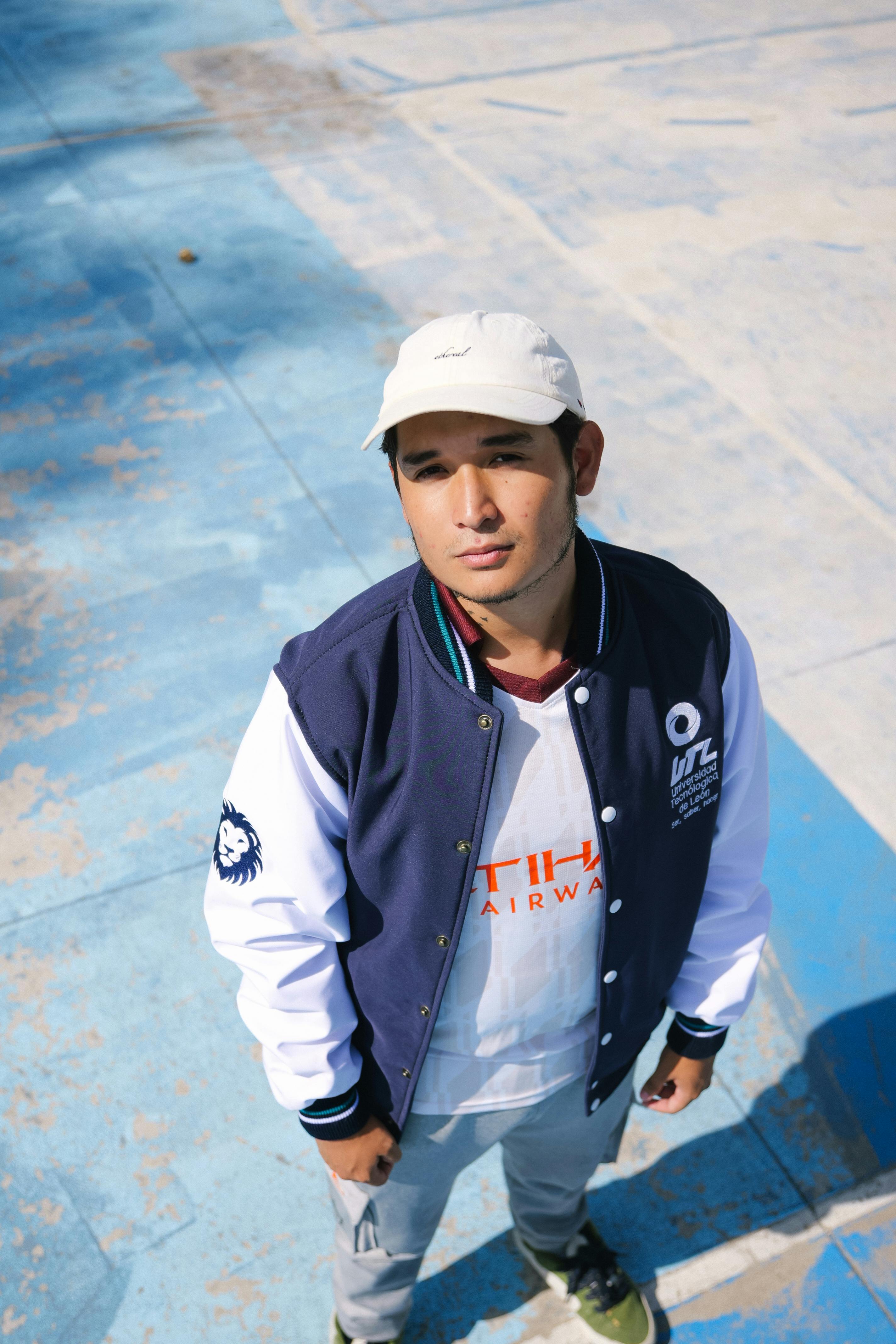 gratis Een informeel portret van een jonge man in León, gekleed in een collegejack en pet op een zonnige dag. Stockfoto