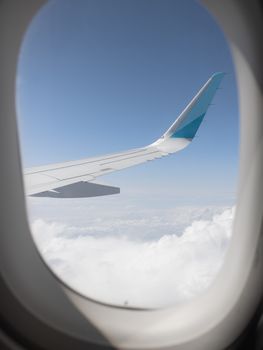 View from an airplane window, showcasing the wing against a bright, clear sky and fluffy clouds.