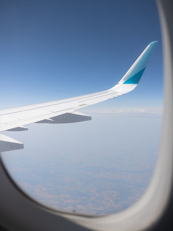 View of airplane wing from window seat during flight with clear blue sky